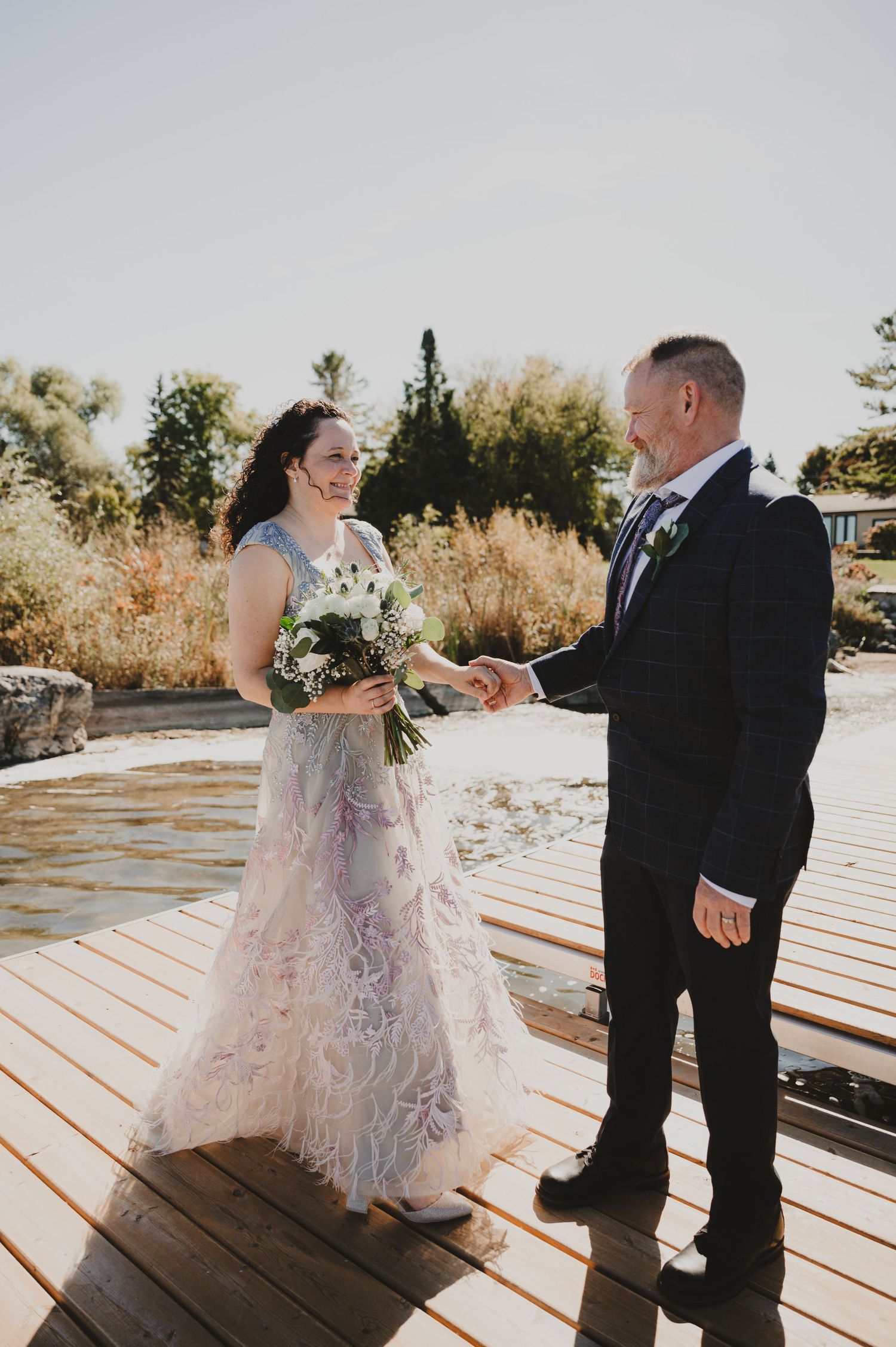 A couple in formal attire shares a romantic dance moment on a wooden deck during a sunset wedding celebration.