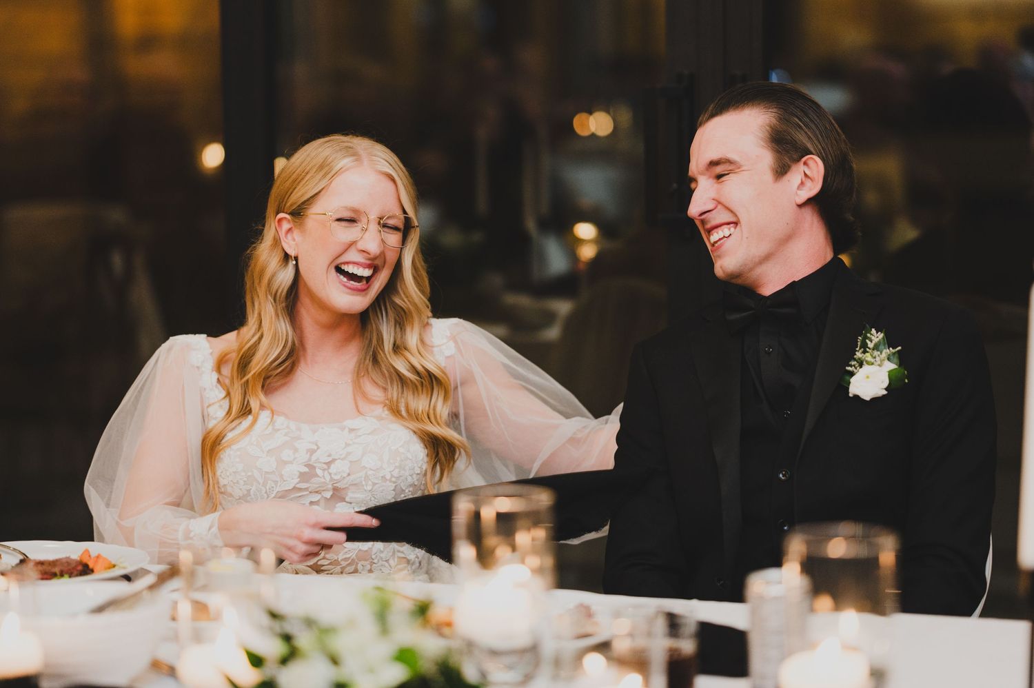 Guests sharing joyful laughter during an elegant evening reception at a dimly lit venue.
