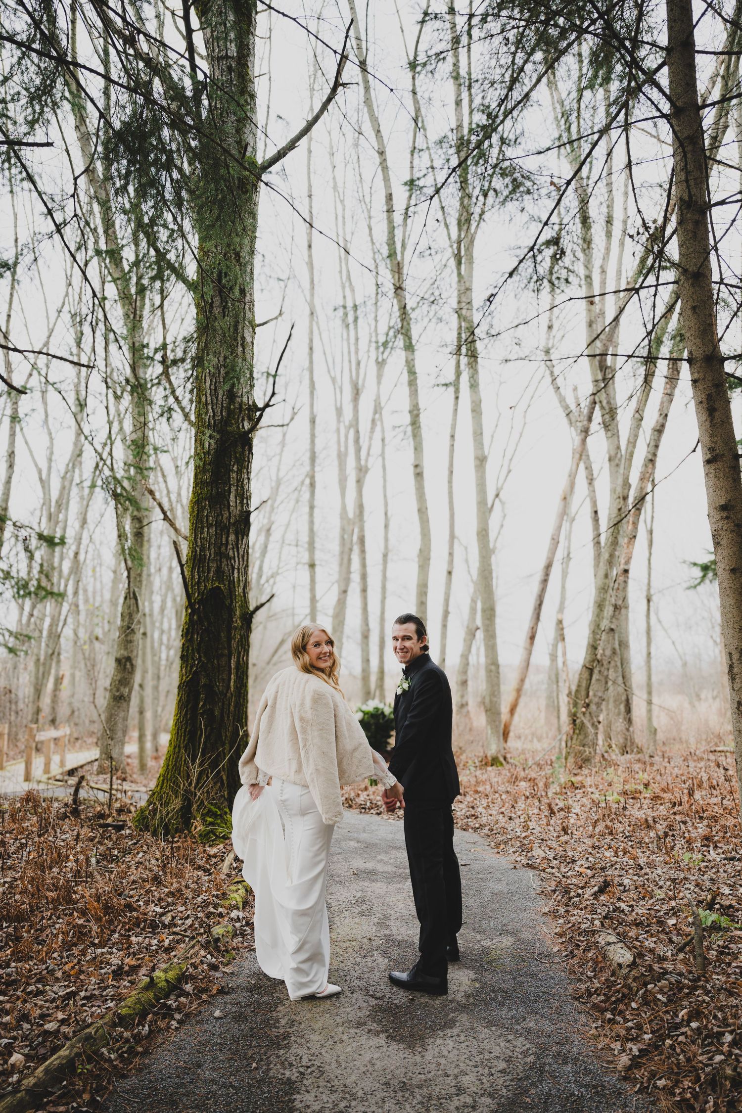 A couple shares an intimate moment in a misty winter forest with bare trees and fallen leaves on the ground.