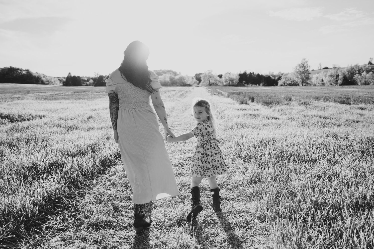 Black and white photograph showing a couple walking together through a sunlit meadow on a summer day.