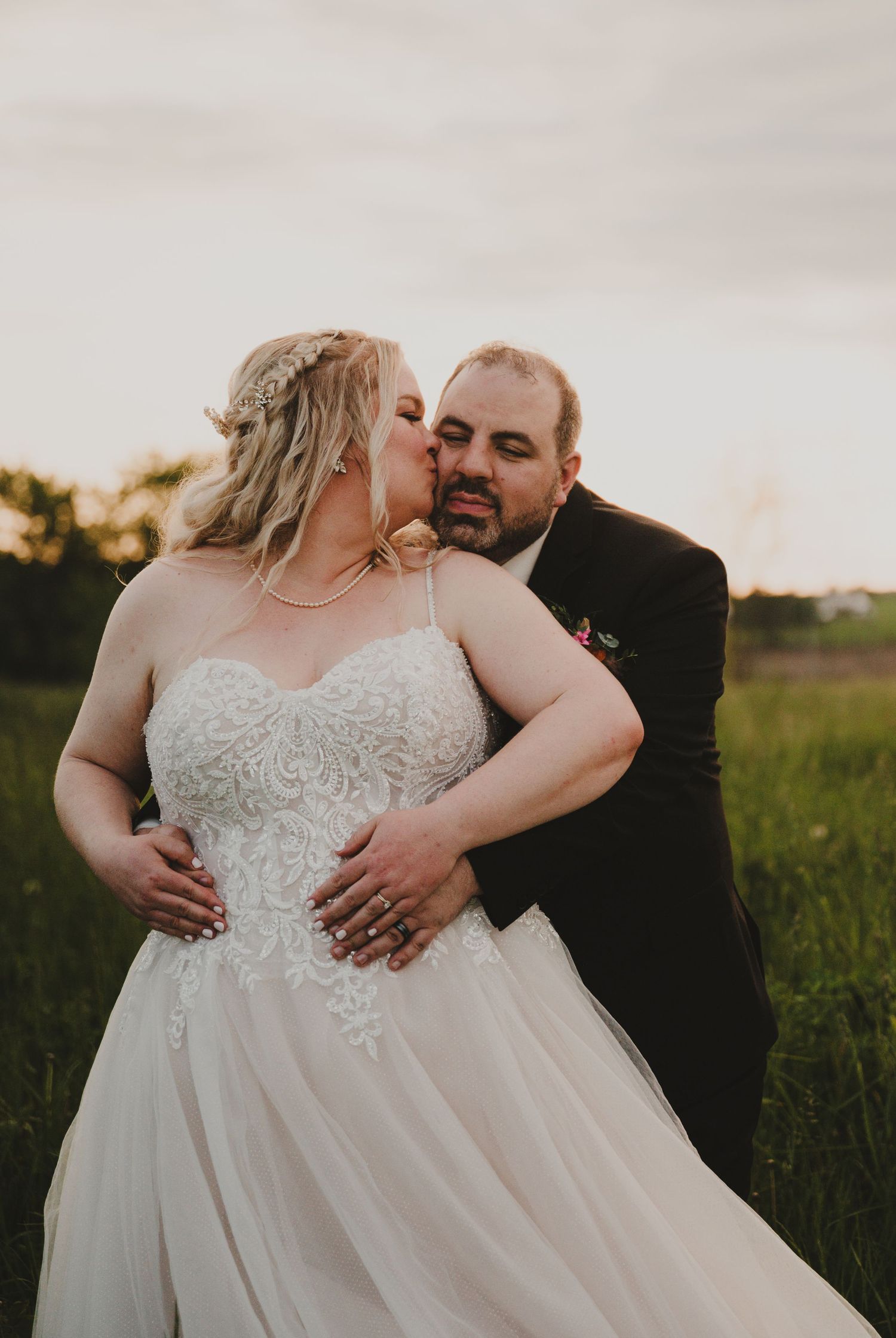 A romantic sunset wedding photoshoot in a field with a couple embracing in formal attire.