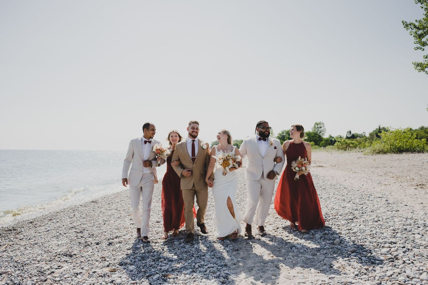 A wedding party walks and poses together on a scenic beach with soft waves and sand in the background.