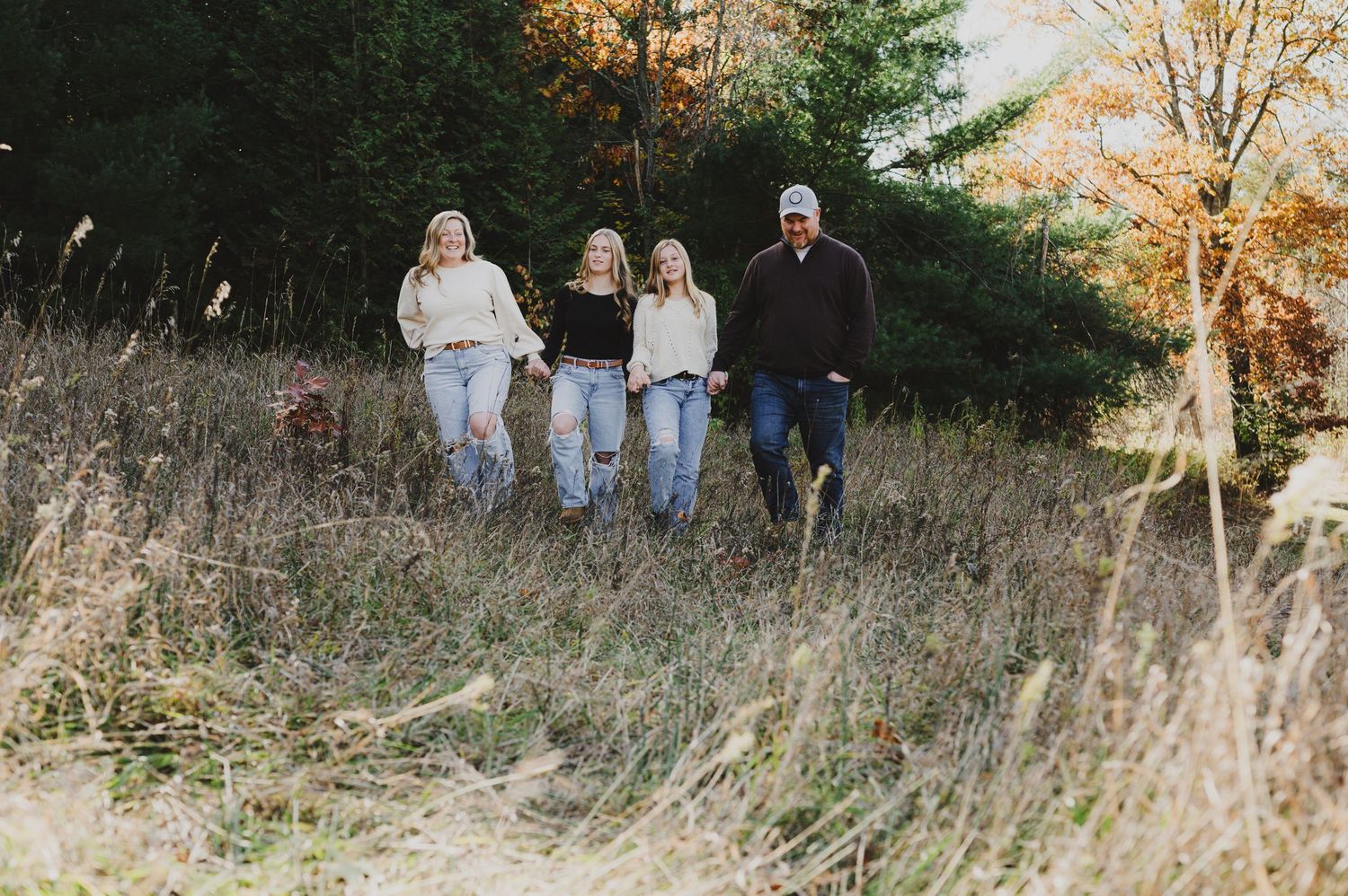 A group walks through tall autumn grass during a golden sunset photo session in a rustic outdoor setting.