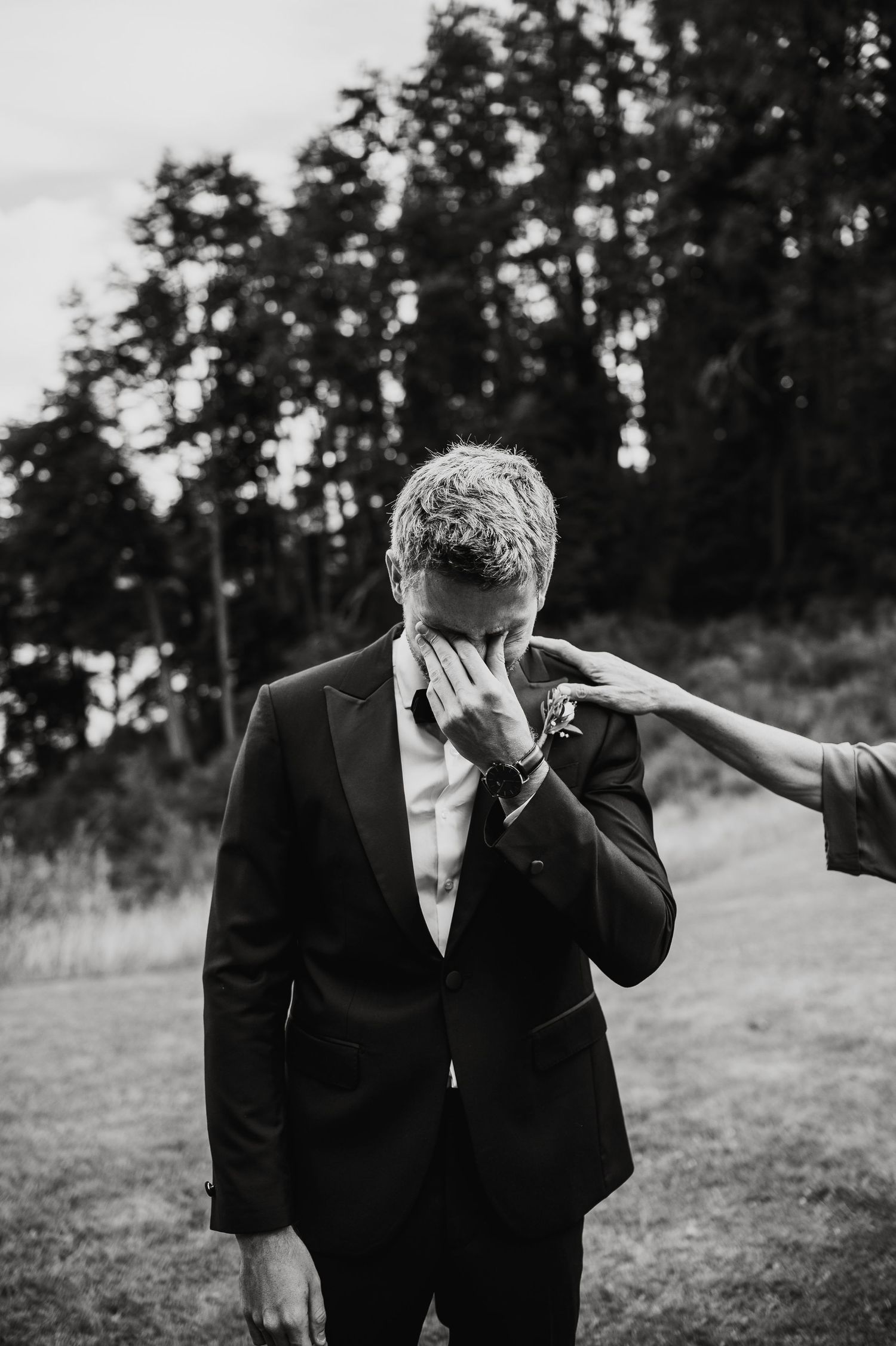 Black and white photo of person in formal suit wiping tears during emotional outdoor moment.