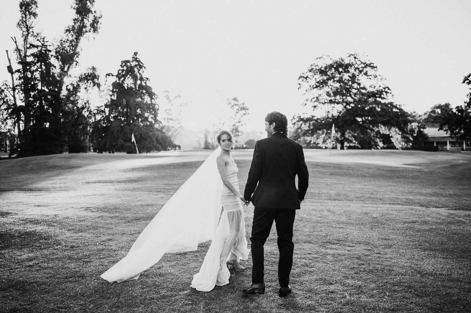 A romantic black and white wedding photo sequence showing a couple walking together in an outdoor field setting.