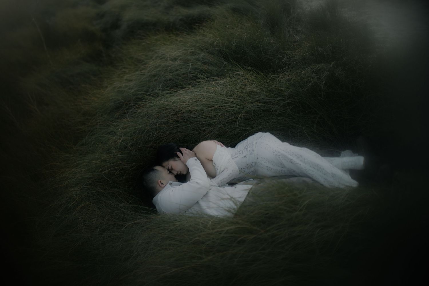 A figure in white lies dramatically on dark ground in a moody setting captured by a destination elopement photographer.