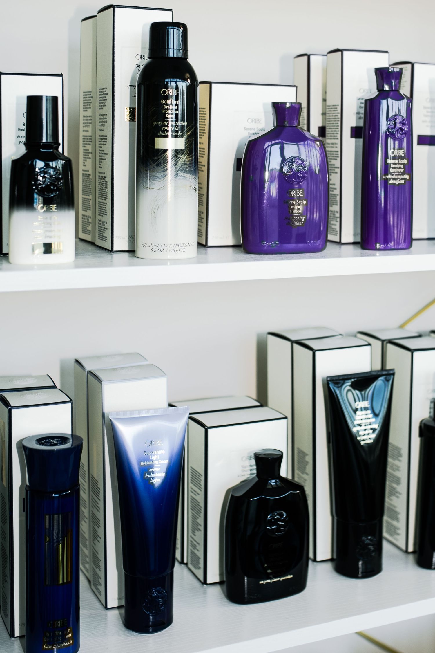 Rows of luxury perfume bottles in black, purple, and silver displayed on white retail shelves.