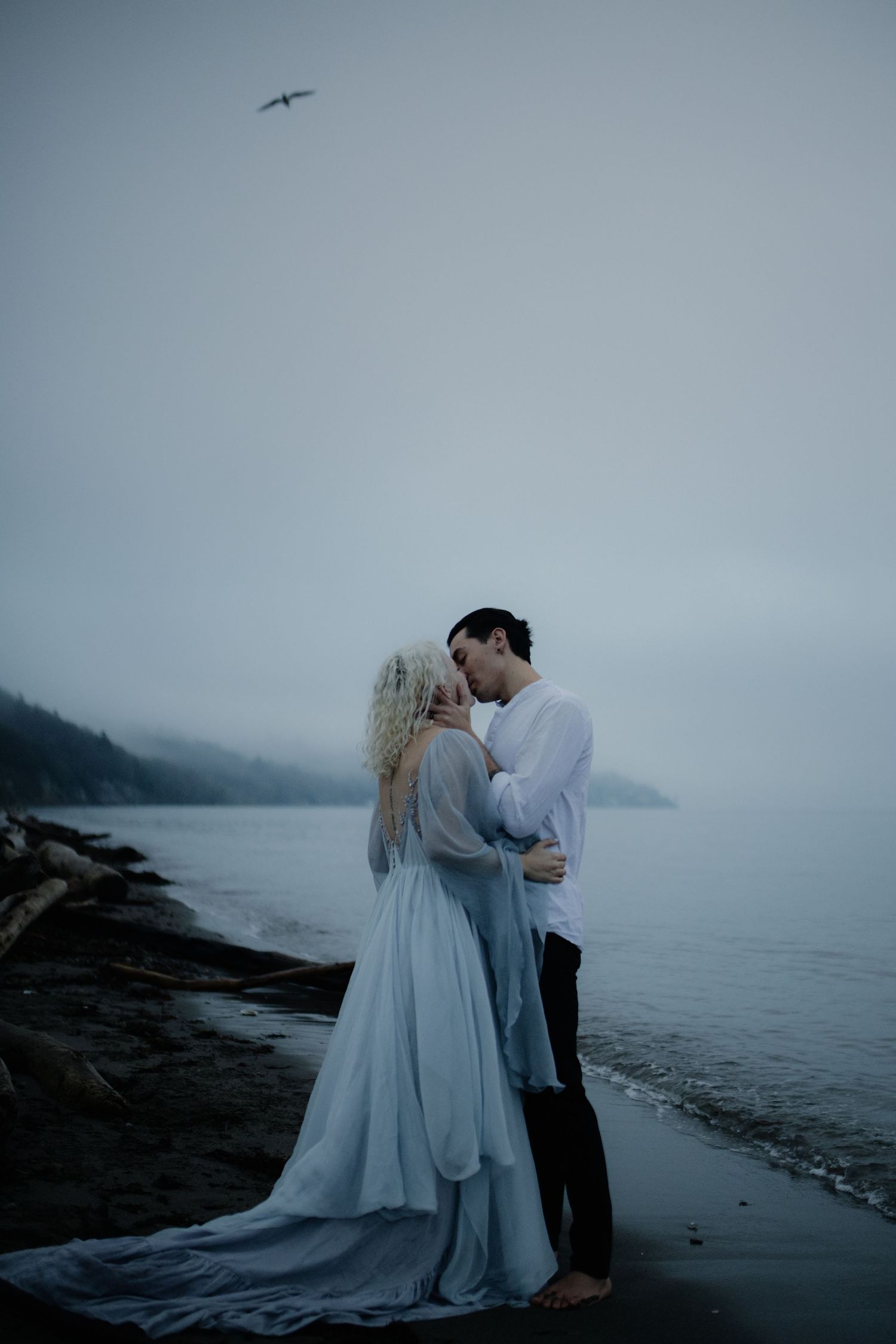 Ethereal beach wedding scene with a couple embracing against a misty coastal backdrop captured by a destination elopement photographer.