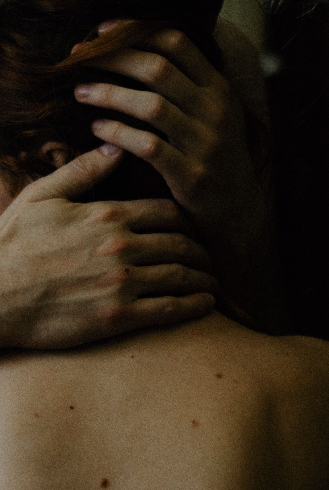 Intimate close-up photograph of hands resting on bare skin in dim lighting captured by a destination elopement photographer.