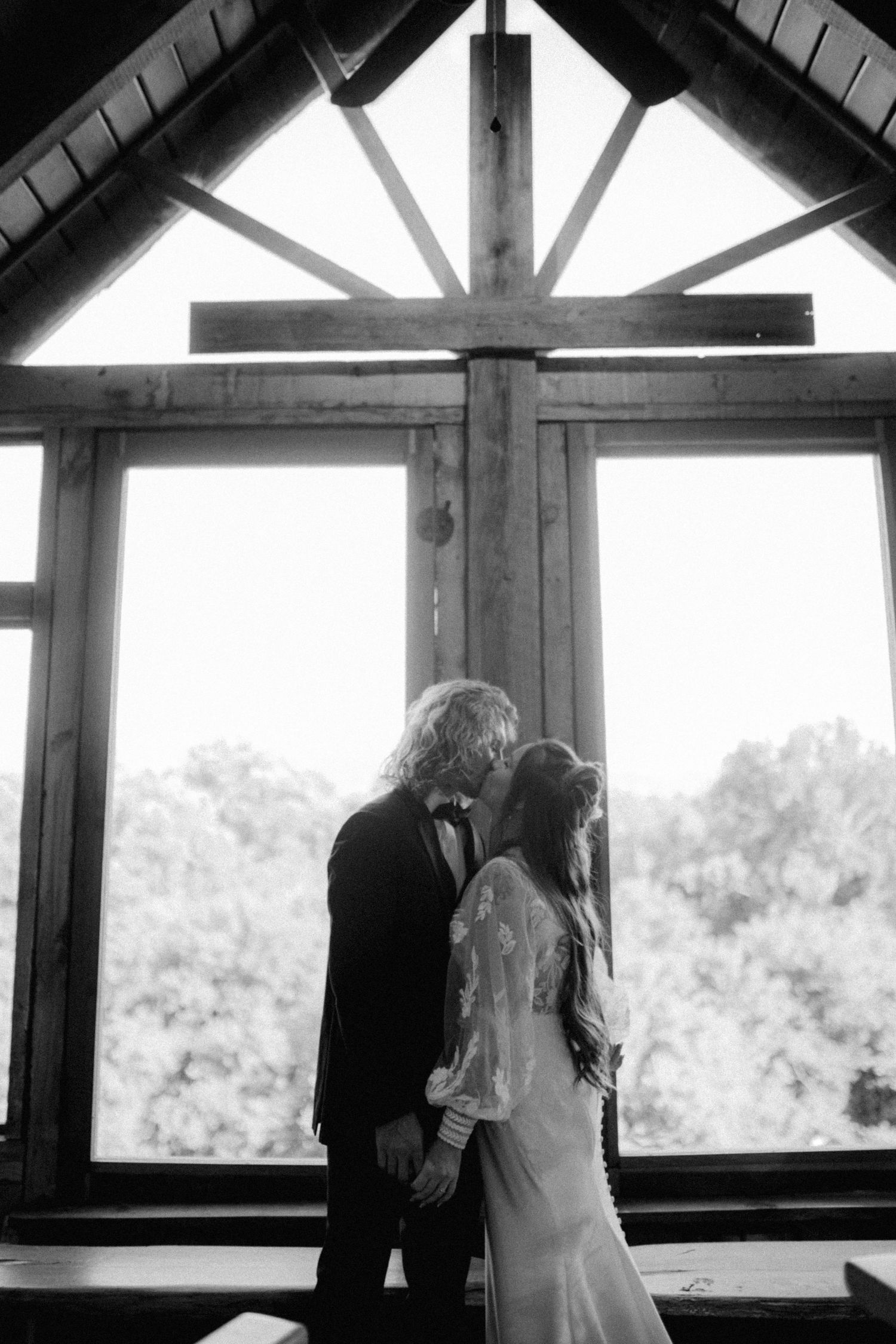 Wedding couple silhouetted against large windows in an architectural setting.