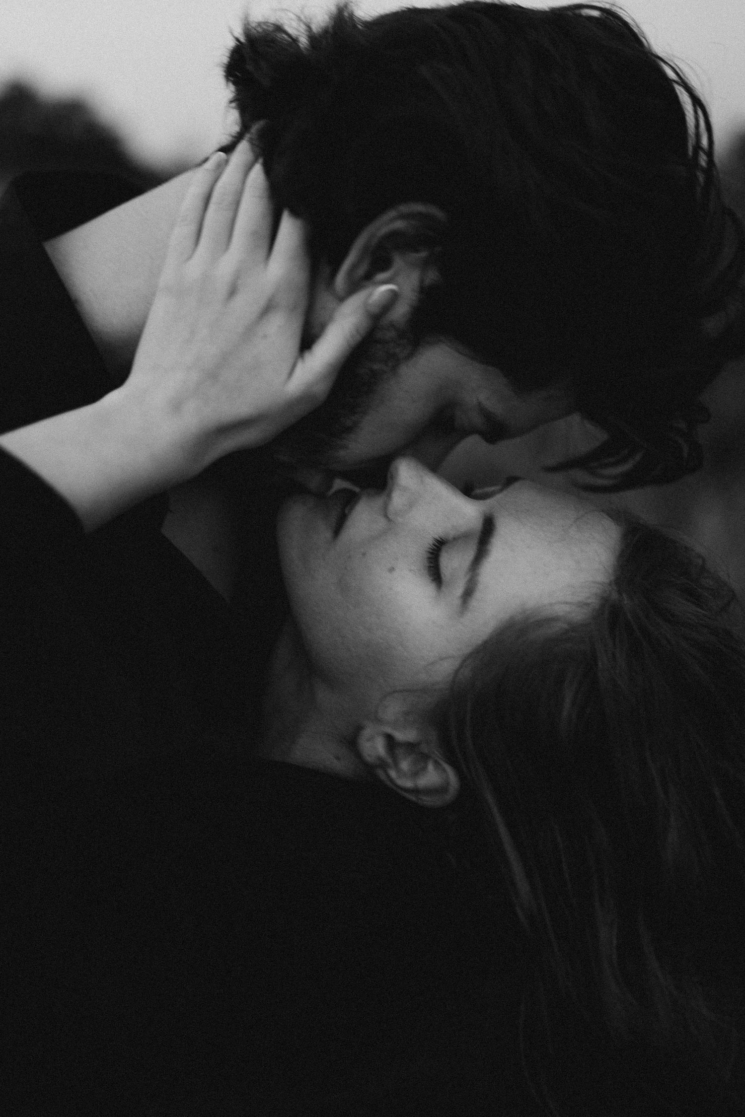 Black and white photo of a romantic couple sharing an intimate kiss, woman with eyes closed and hand on mans head.