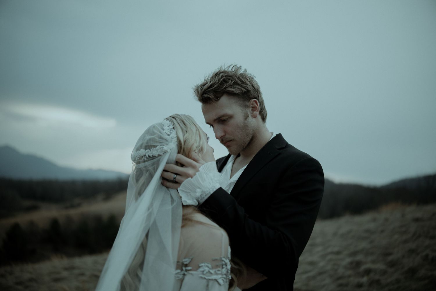 A bride and groom share an intimate moment outdoors, with misty mountains in the background on their wedding day.
