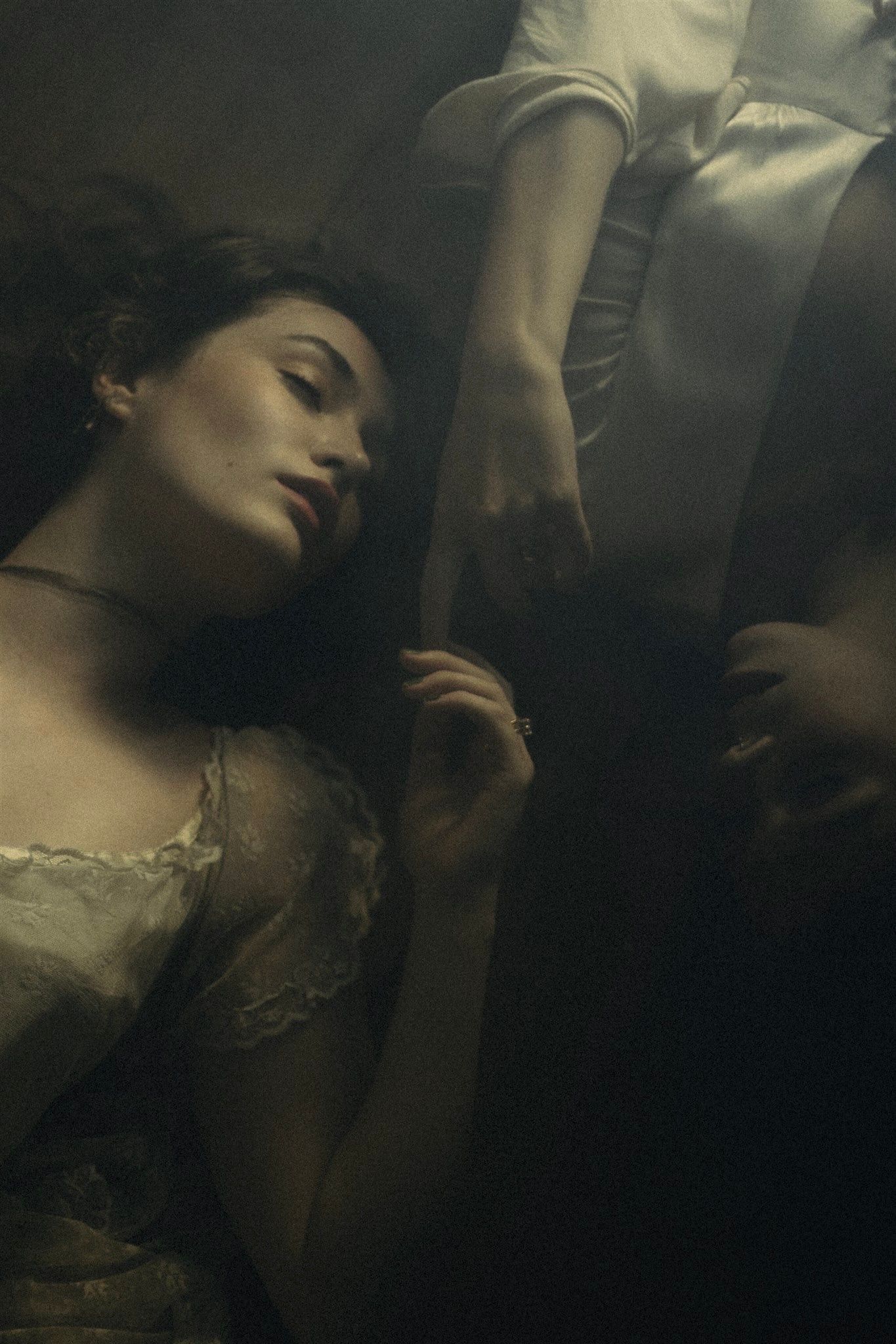 Atmospheric portrait in dark moody lighting shows figure in vintage lace dress with dramatic shadows and ethereal pose.