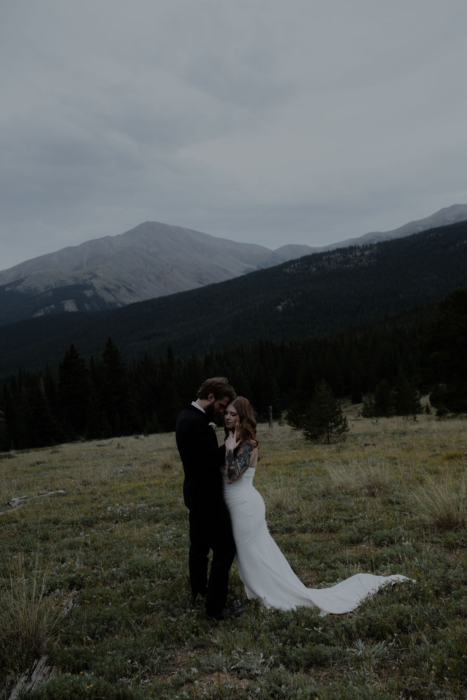 A wedding couple poses dramatically against a mountain backdrop at dusk.