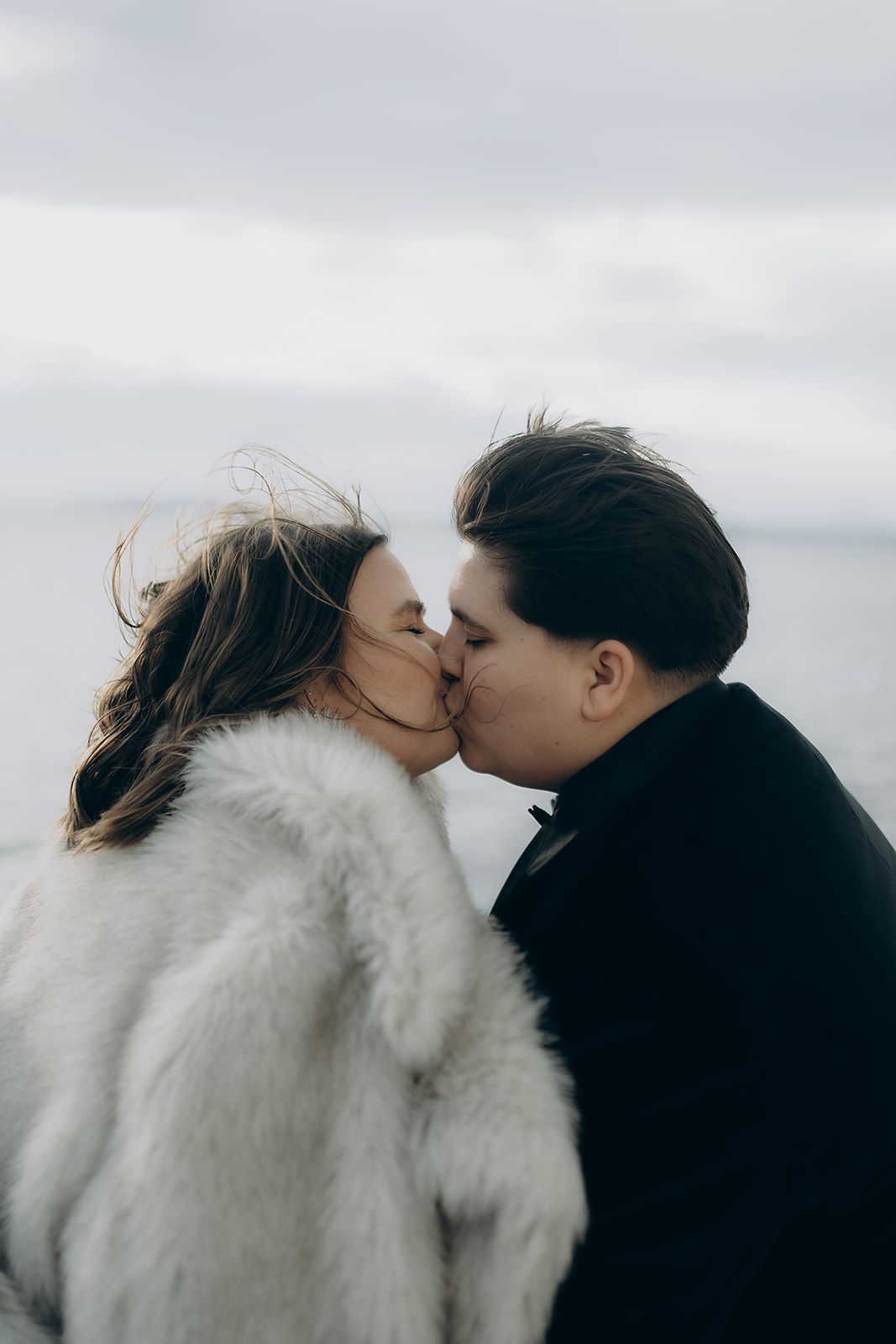 Two people share an intimate kiss against a cloudy sky backdrop in a series of romantic black and white photographs.