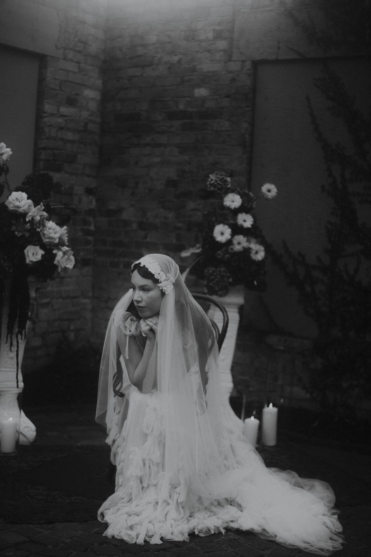 Dramatic black and white bridal portrait with flowing veil against a brick wall.
