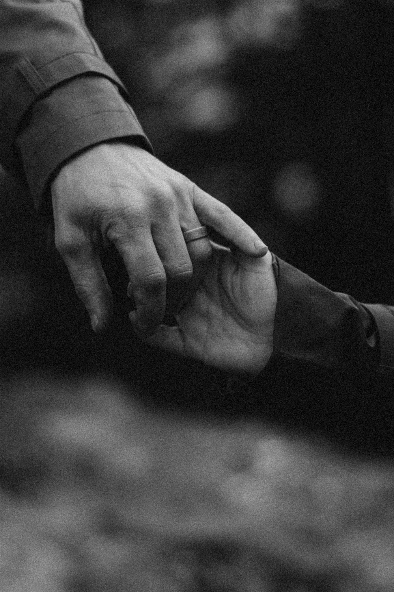 Black and white close-up of hands reaching toward each other in dramatic lighting.