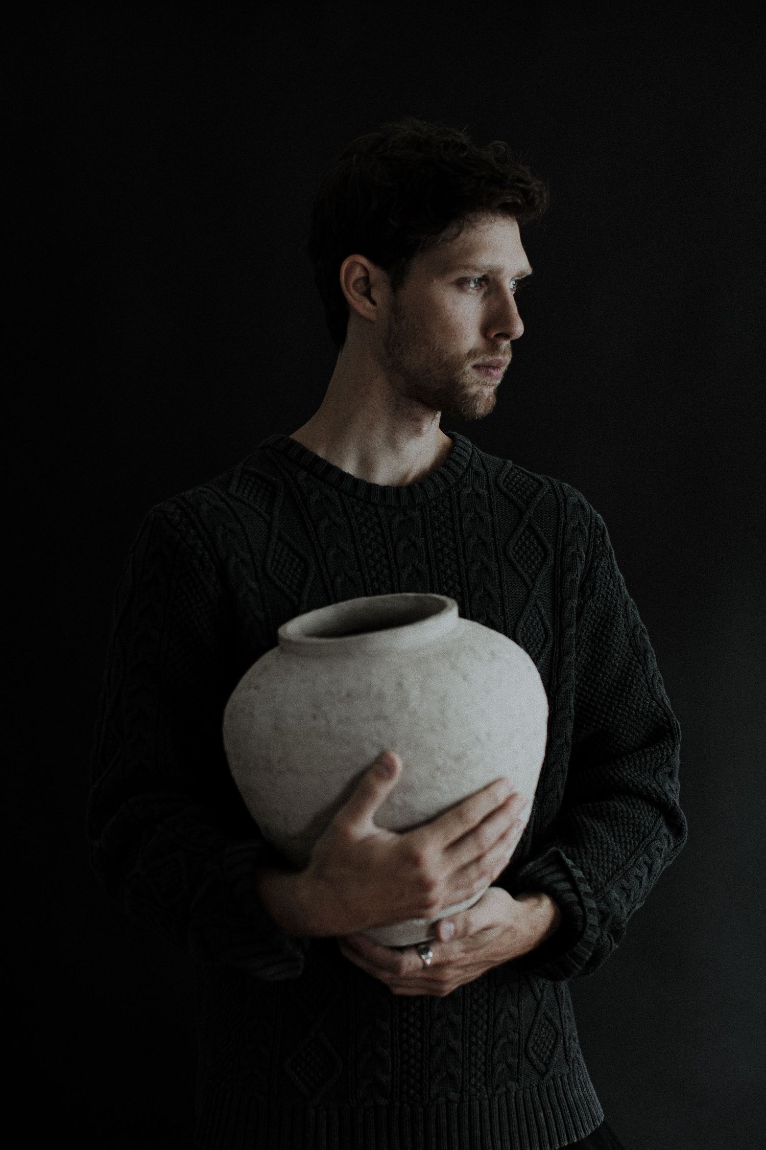 Dramatic series of photos showing hands holding a white ceramic vessel against dark background in moody lighting.