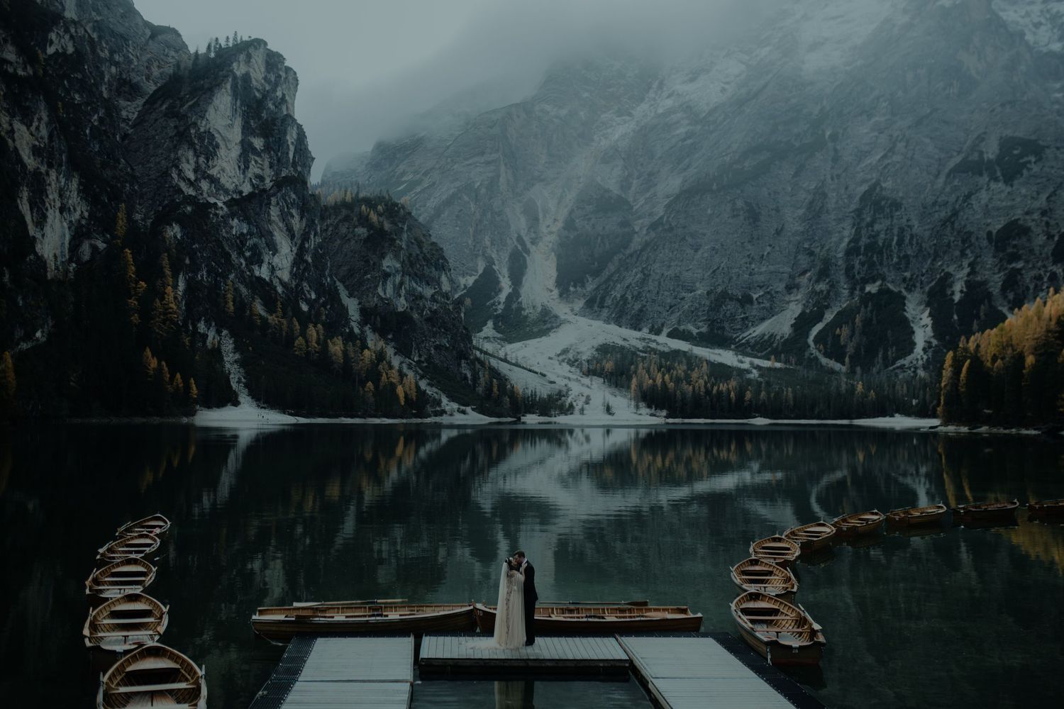 Scenic mountain lake with dramatic peaks and winding road visible in the distance.