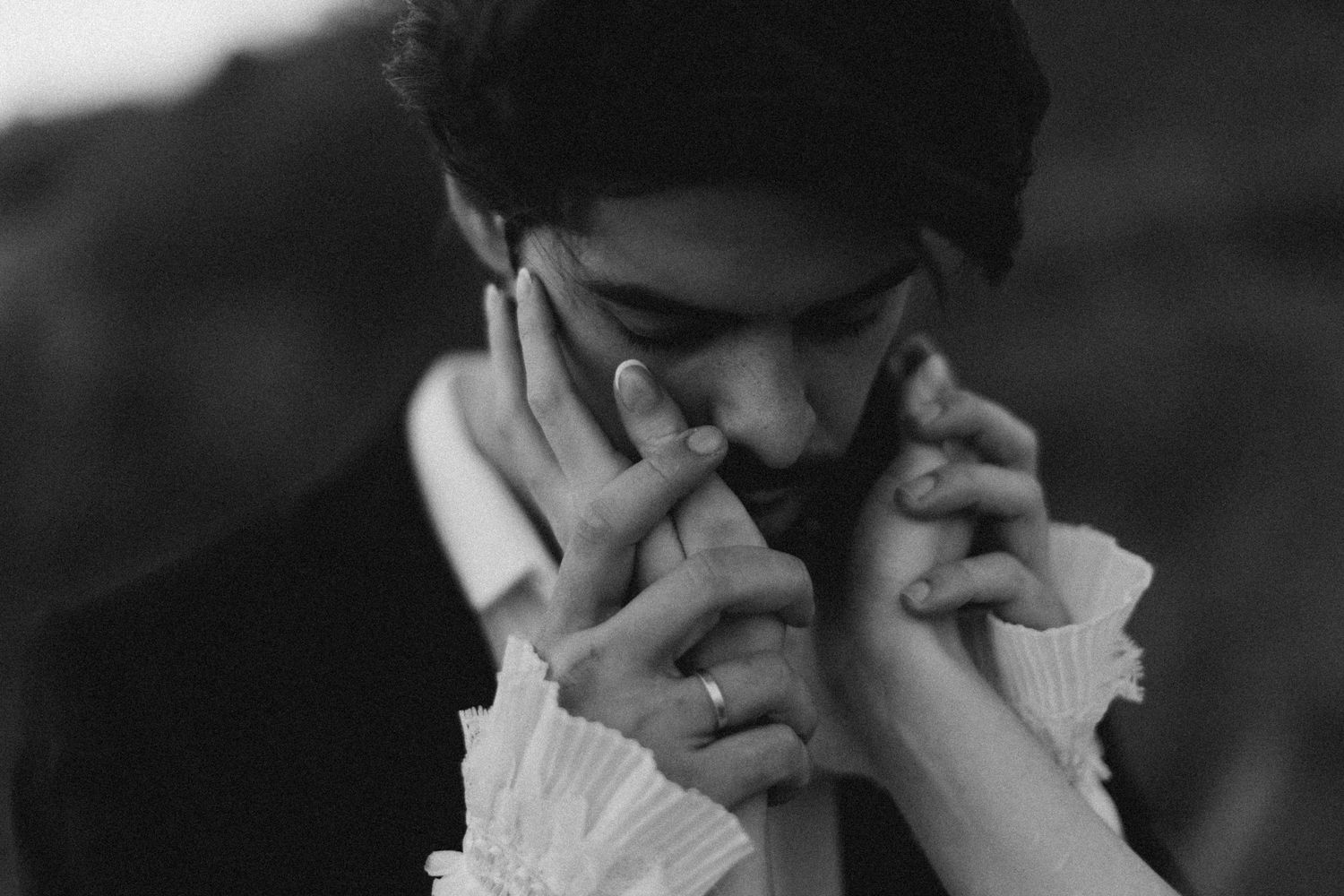 Black and white romantic photo of a groom kissing a bride's hands tenderly during a wedding ceremony.