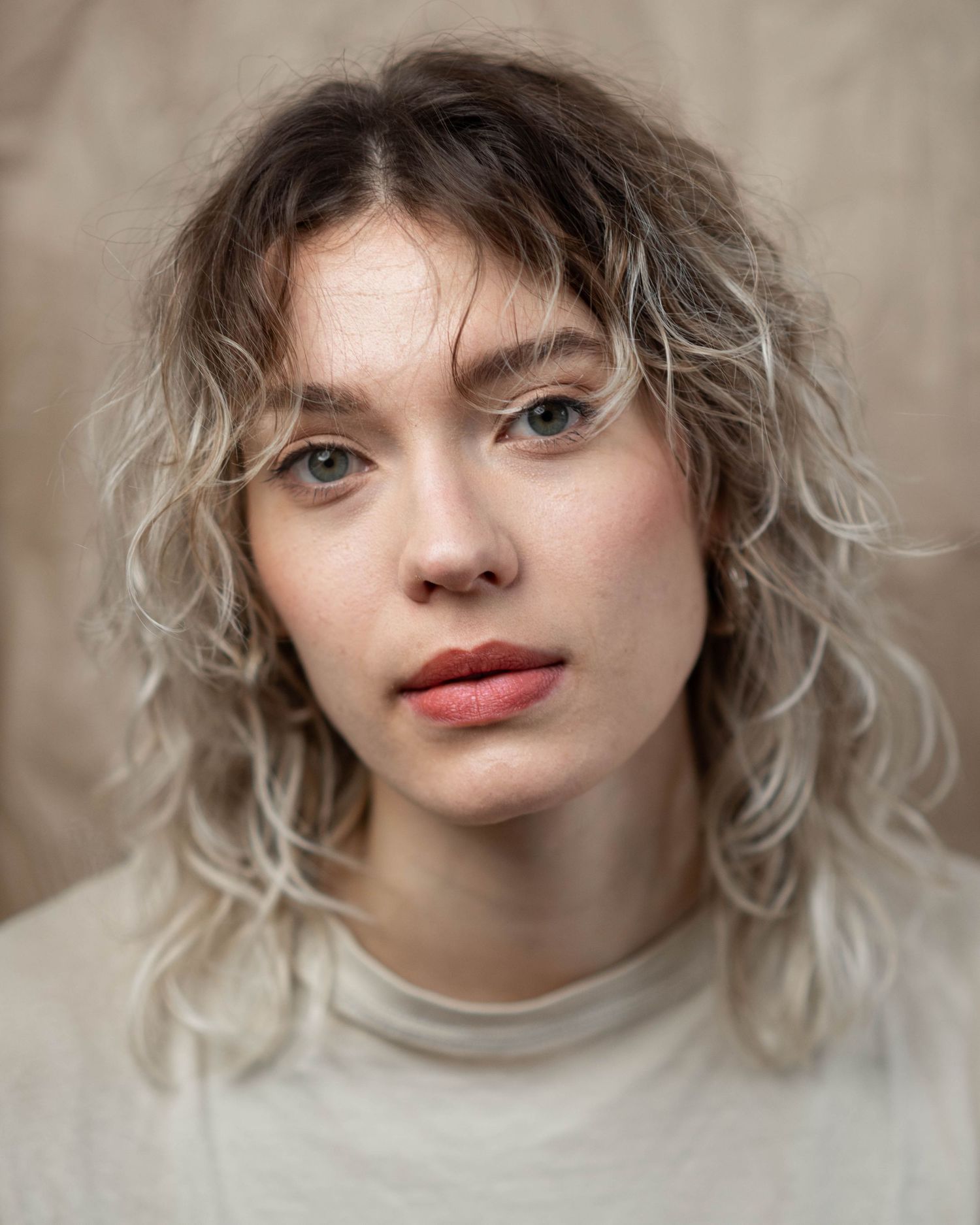 Artistic portrait featuring blonde wavy hair and natural makeup against a neutral backdrop.