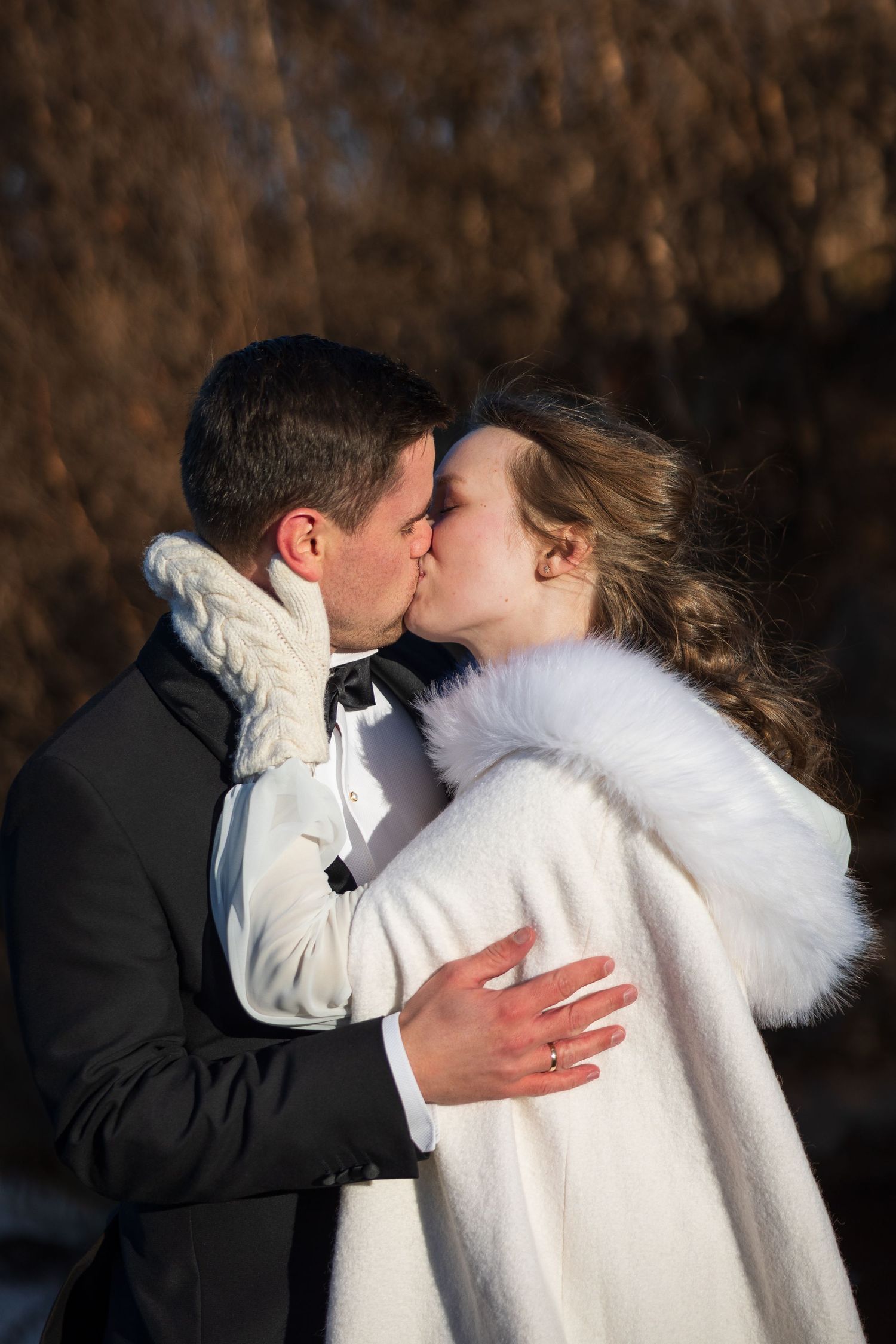 Romantic winter wedding portrait of couple kissing while wrapped in elegant white fur coat.