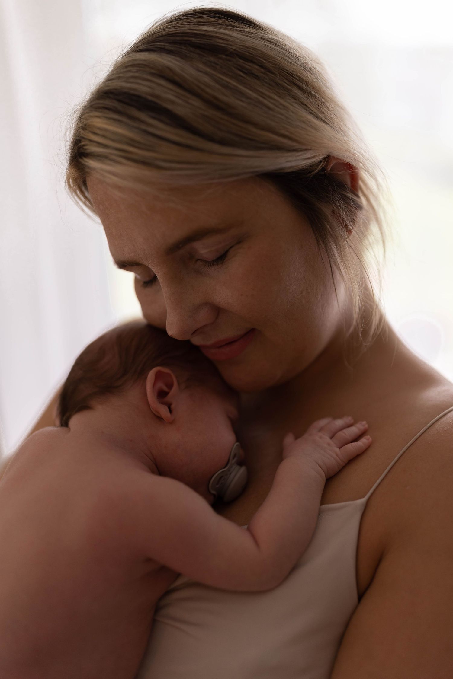 Tender moment between parent and newborn in soft natural window light.