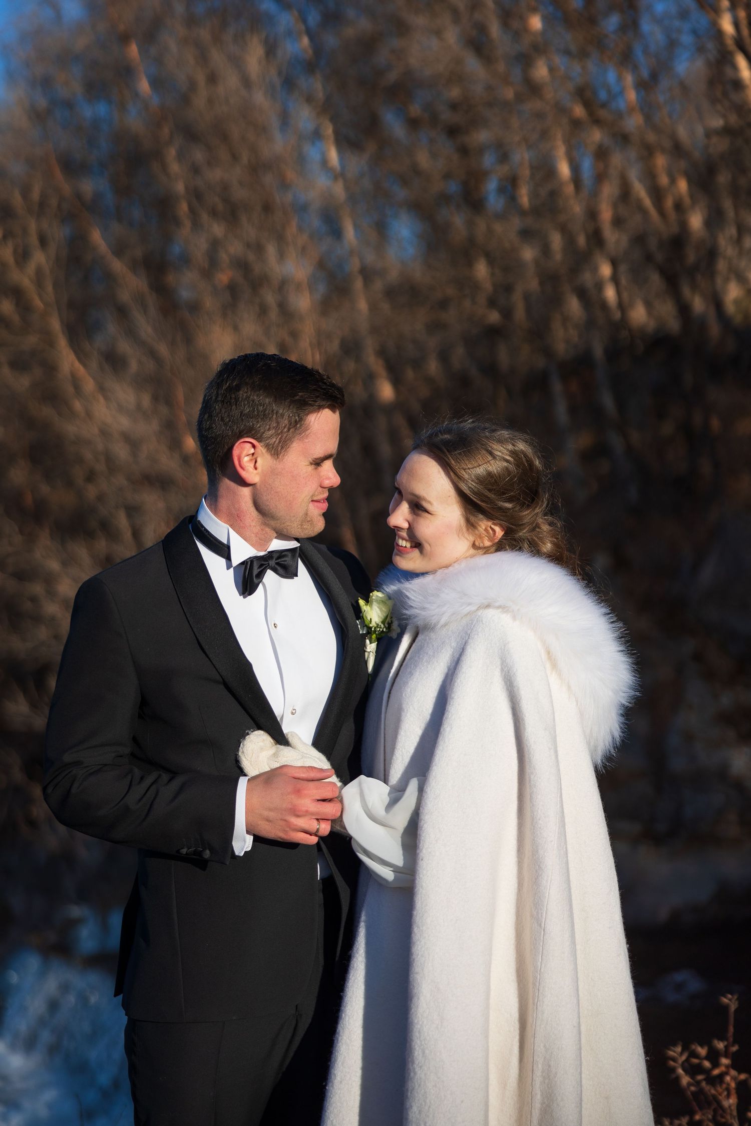 Winter wedding couple in formal attire and white fur coat share intimate moment in snowy setting.