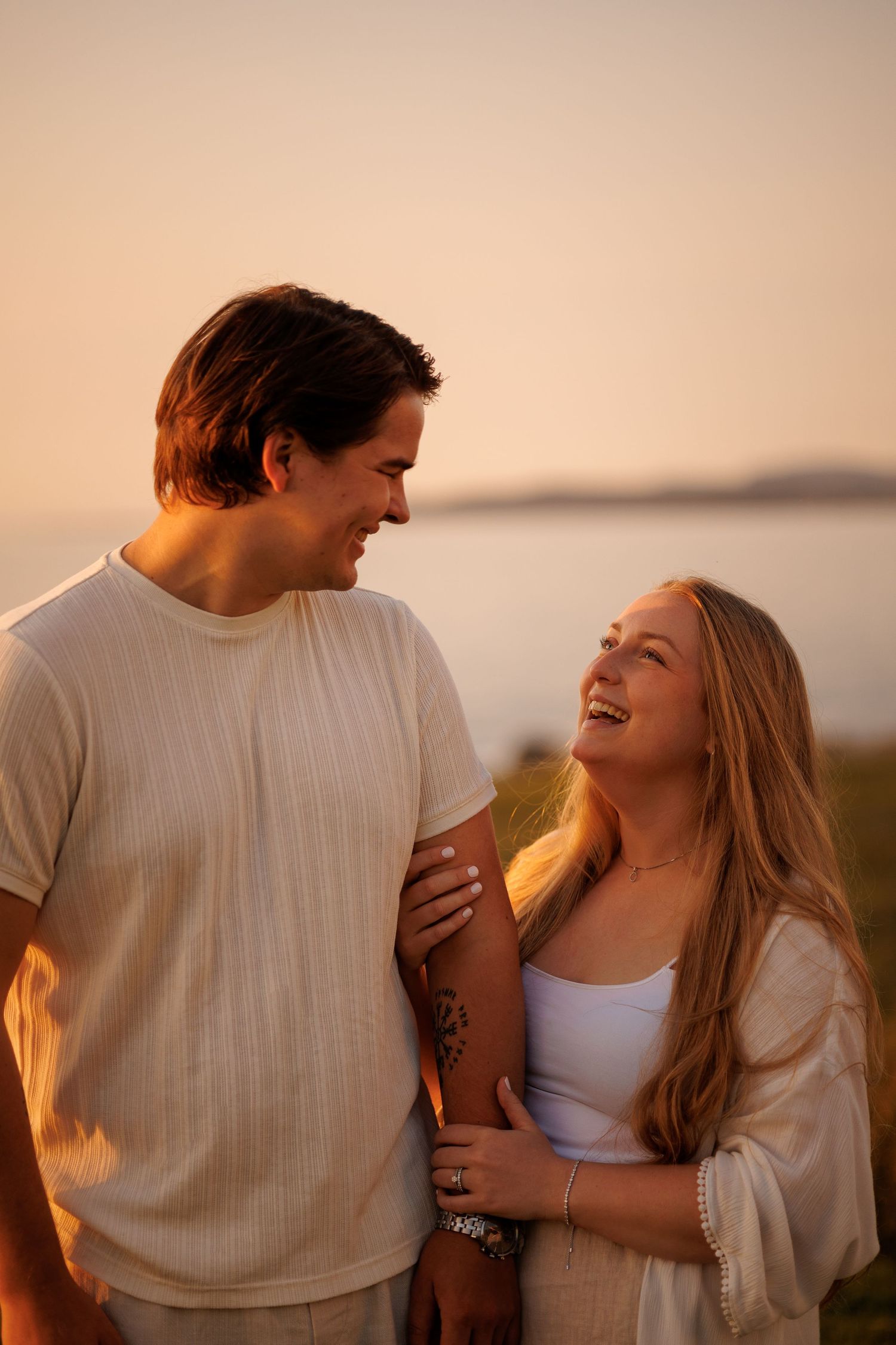 A couple shares intimate laughs together during golden hour sunset in a romantic outdoor setting.