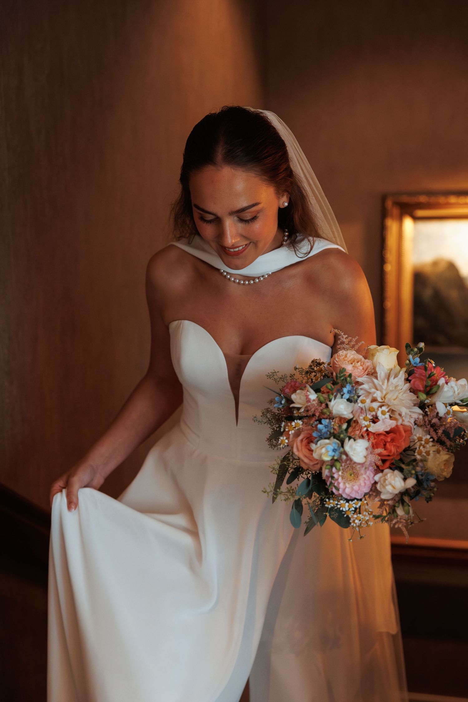 Wedding bouquet with coral and white flowers complements an elegant white bridal gown in warm lighting.