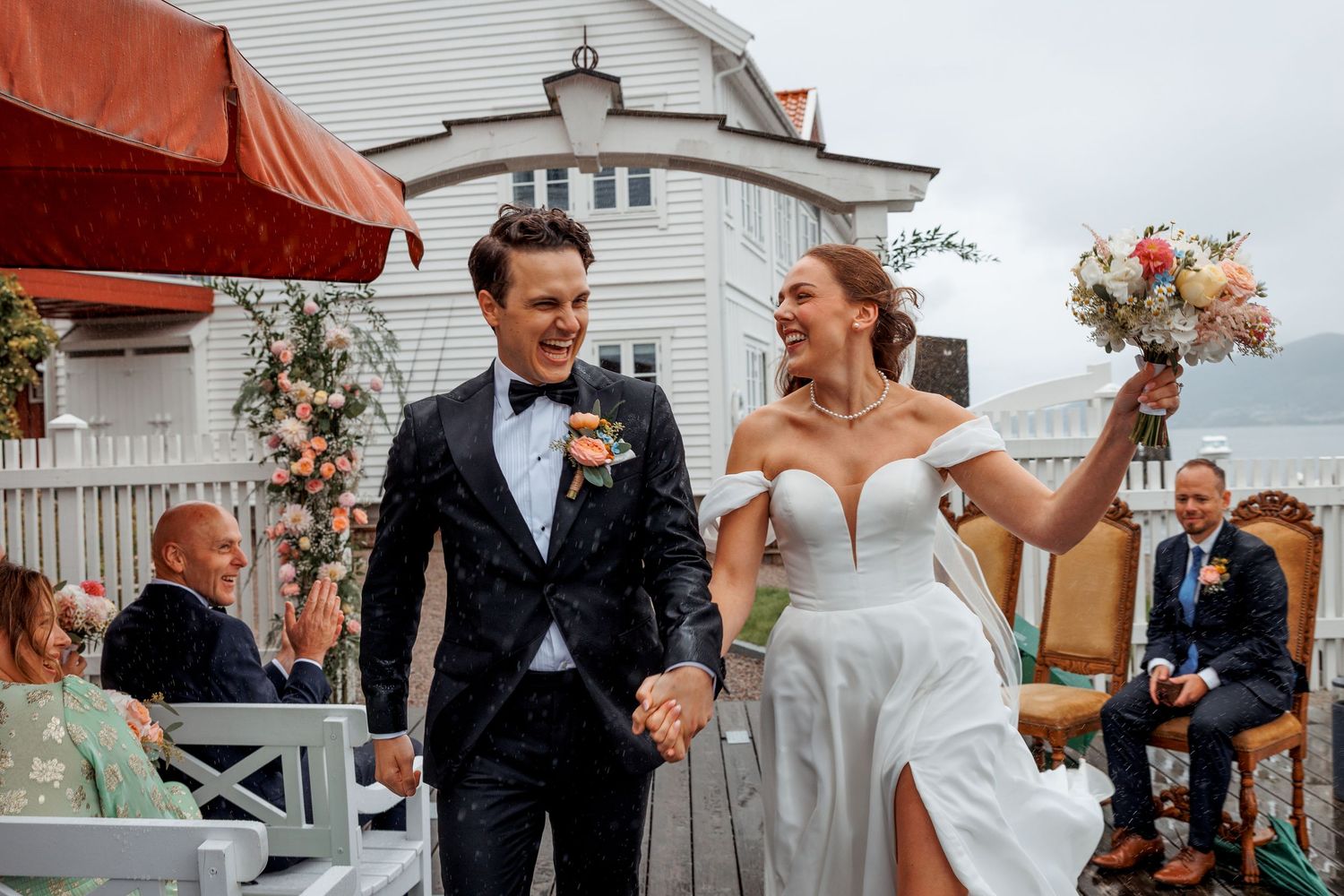 Joyful newlyweds walk hand in hand after outdoor wedding ceremony, bride in white gown raising bouquet.