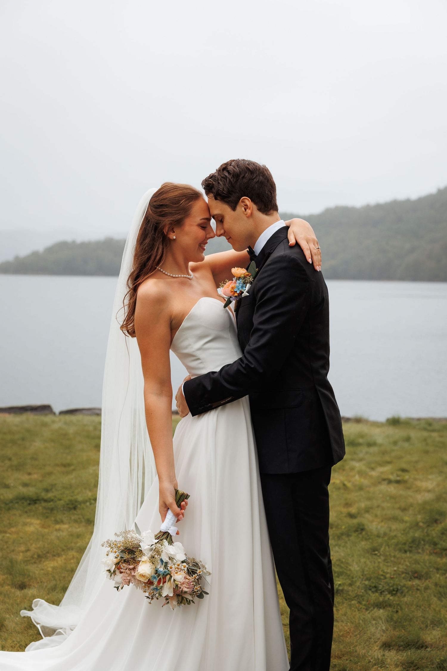 A romantic wedding couple shares intimate moments in front of a misty lakeview landscape.
