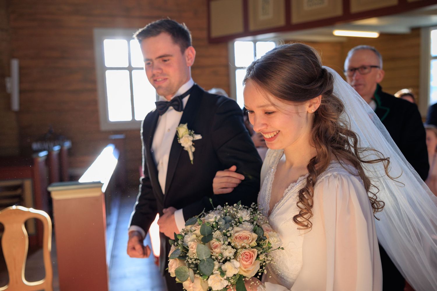 A wedding ceremony inside a wooden church with a bride holding a beautiful bouquet of flowers.