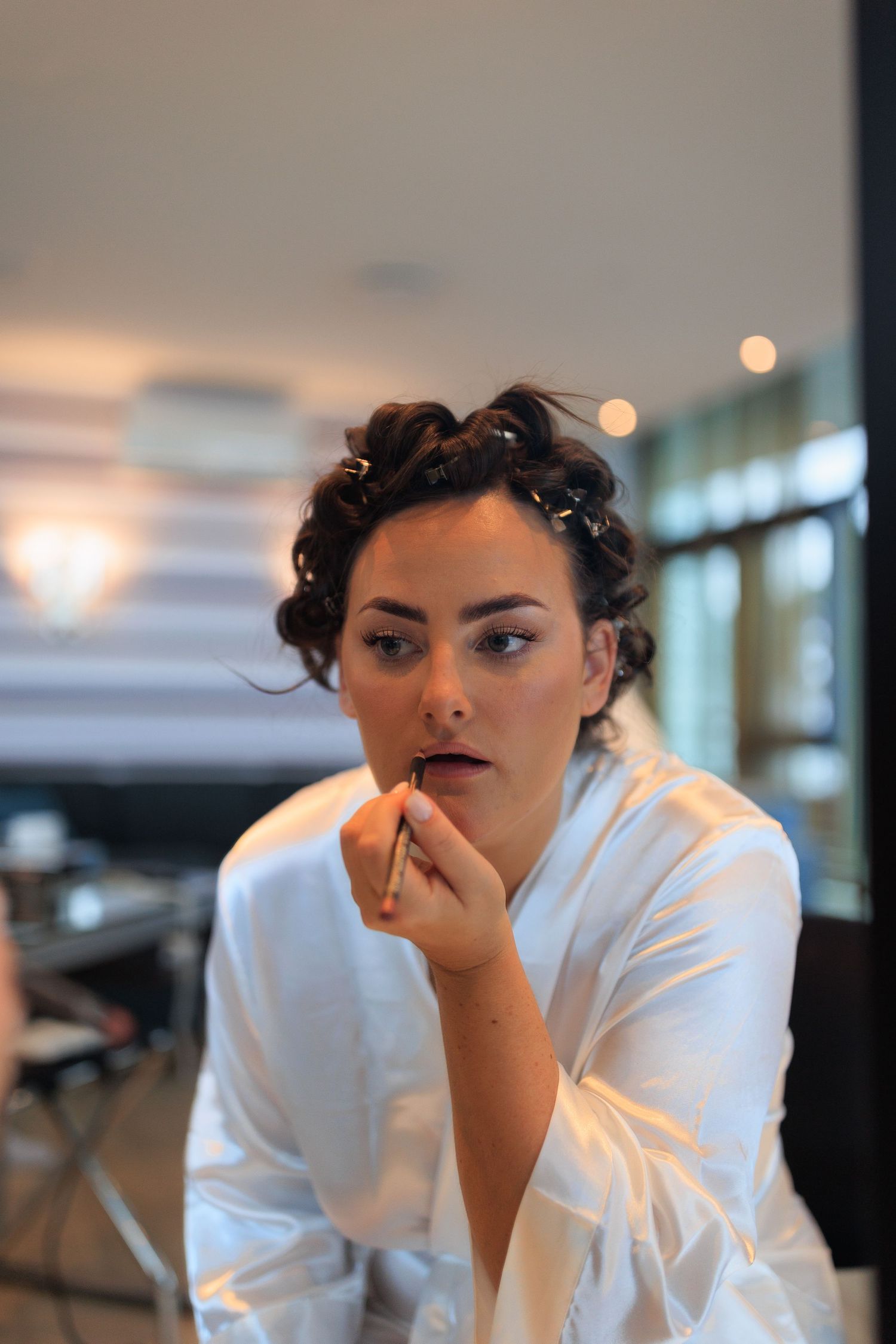 A woman in a white robe applying makeup with styled dark hair.