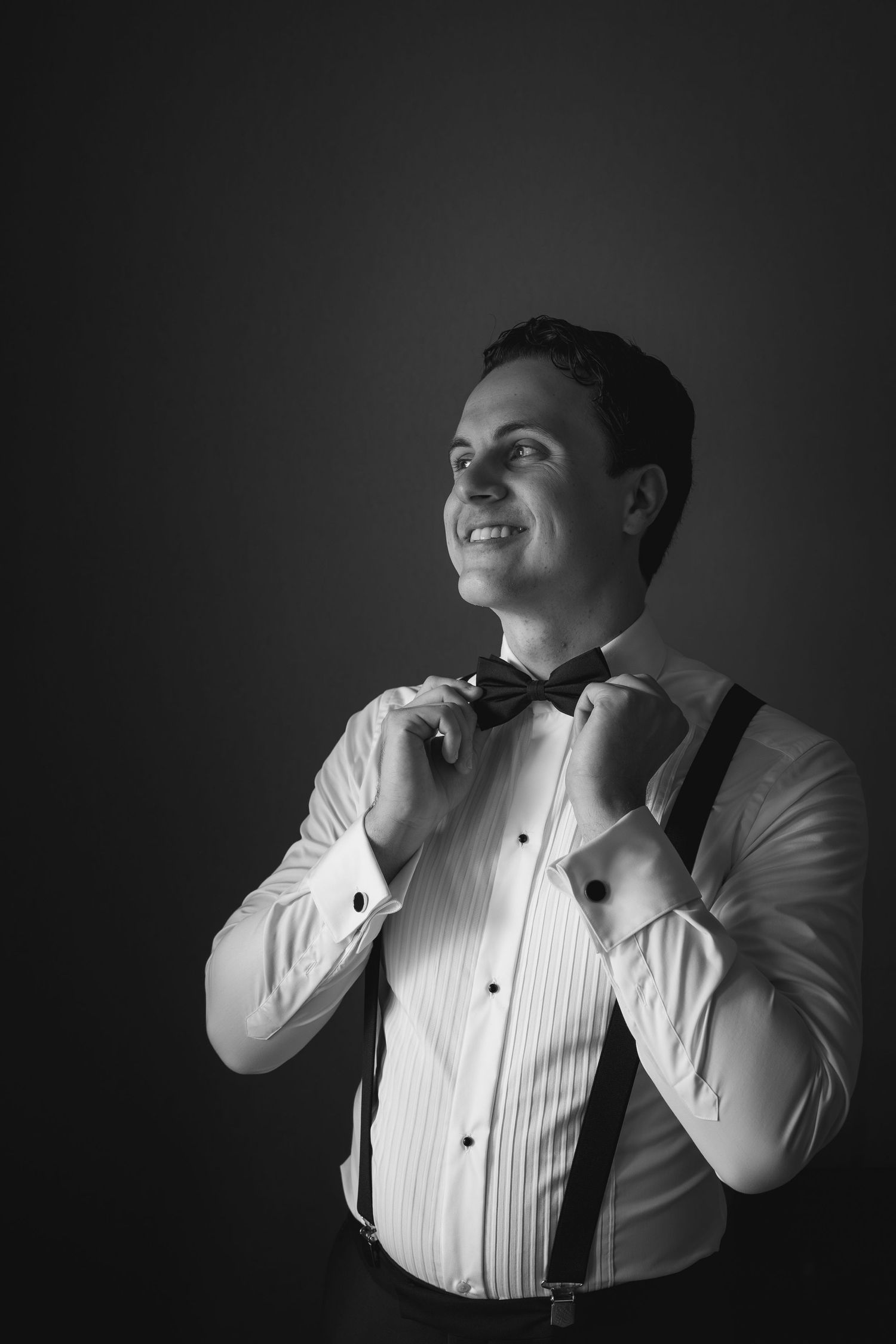 A sequence of black and white photos showing someone adjusting a bow tie while wearing a formal white pleated shirt.
