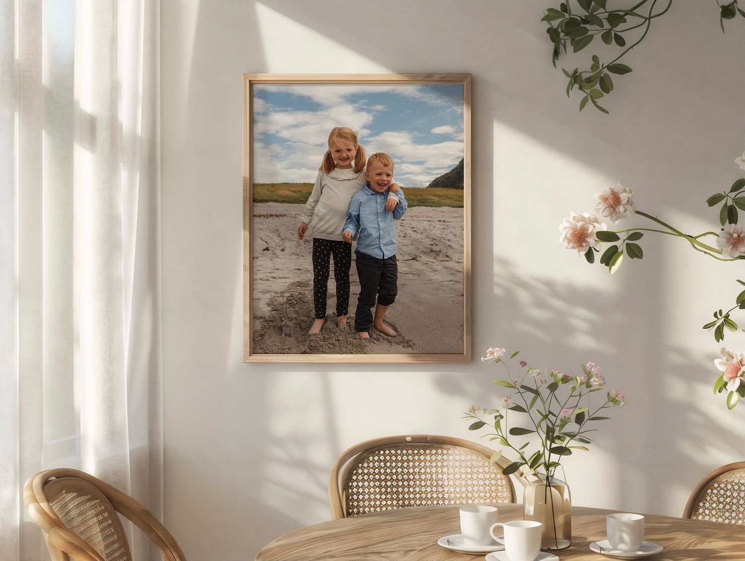 A framed beach portrait hangs on a white wall above a dining area with rattan chairs and delicate floral decor.