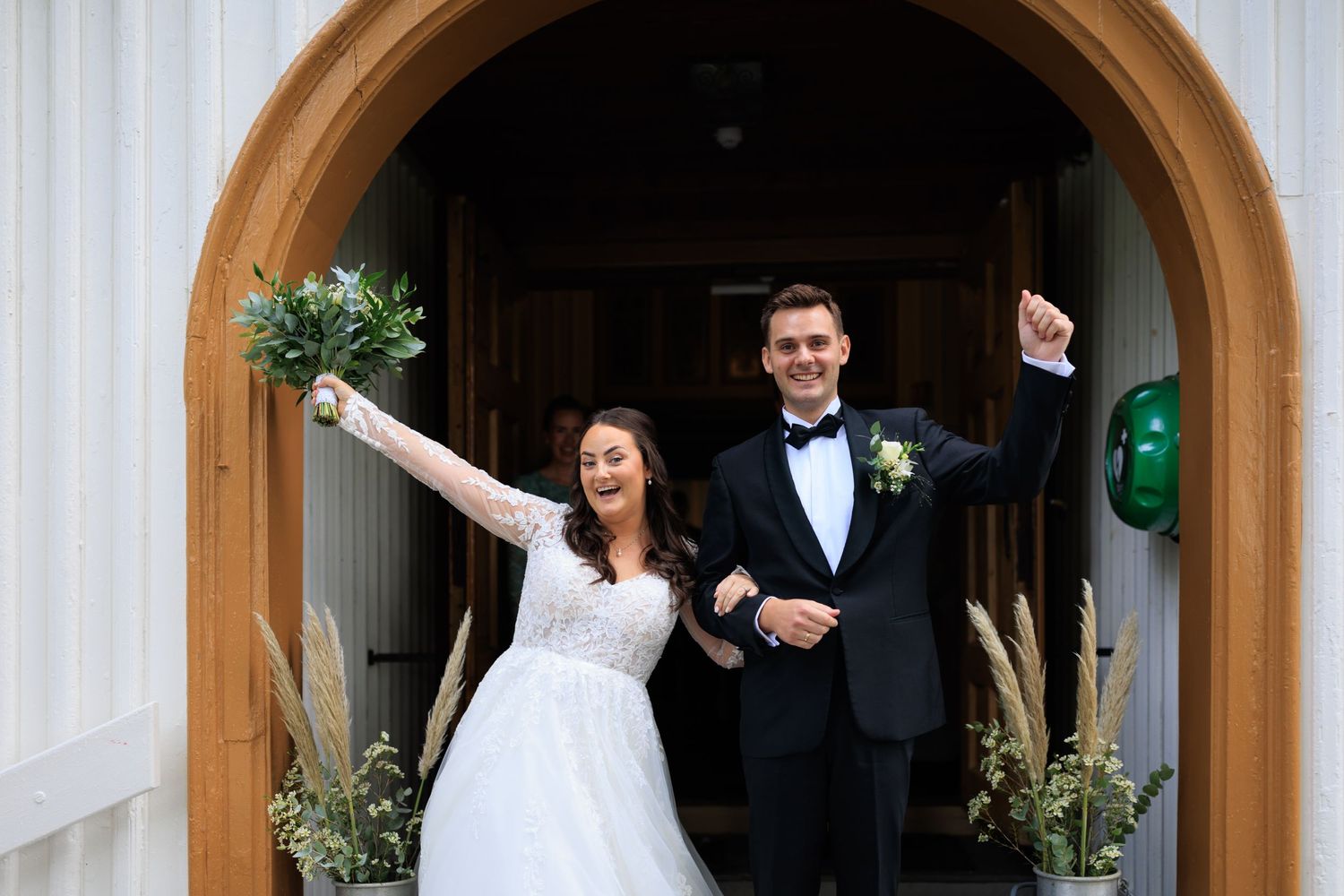 A joyful couple celebrates while exiting through an arched doorway after their wedding ceremony.