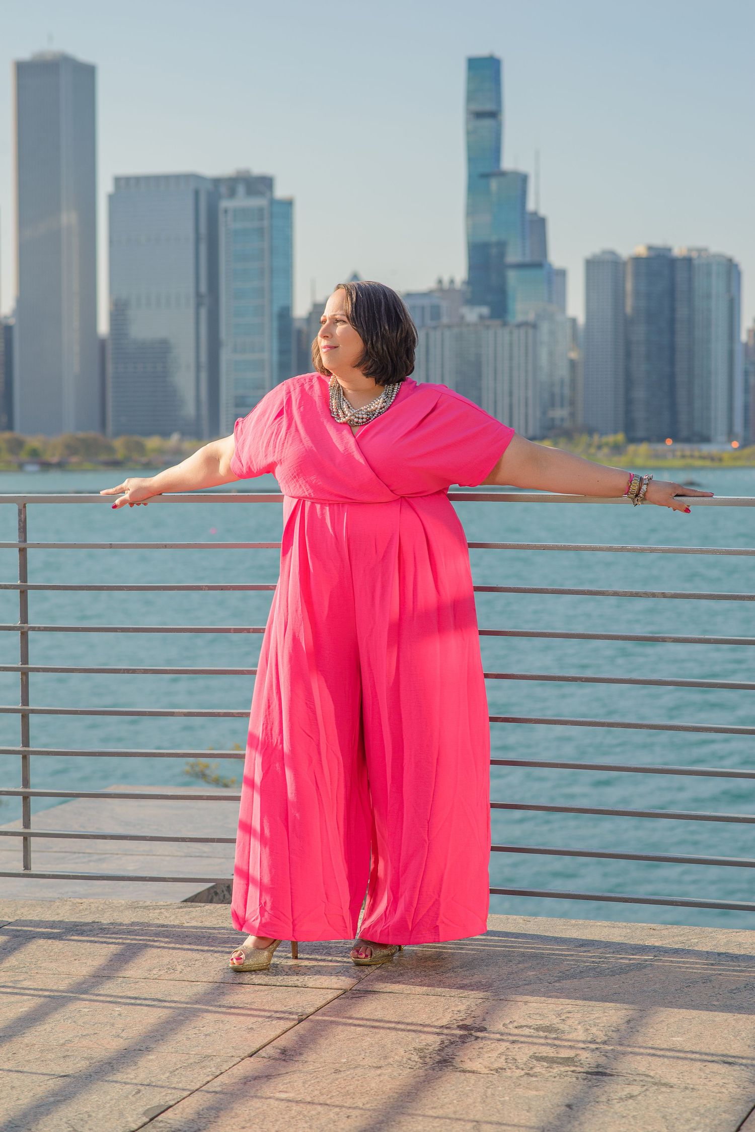 Person in flowing bright pink dress poses gracefully against Chicago skyline and Lake Michigan waterfront backdrop.