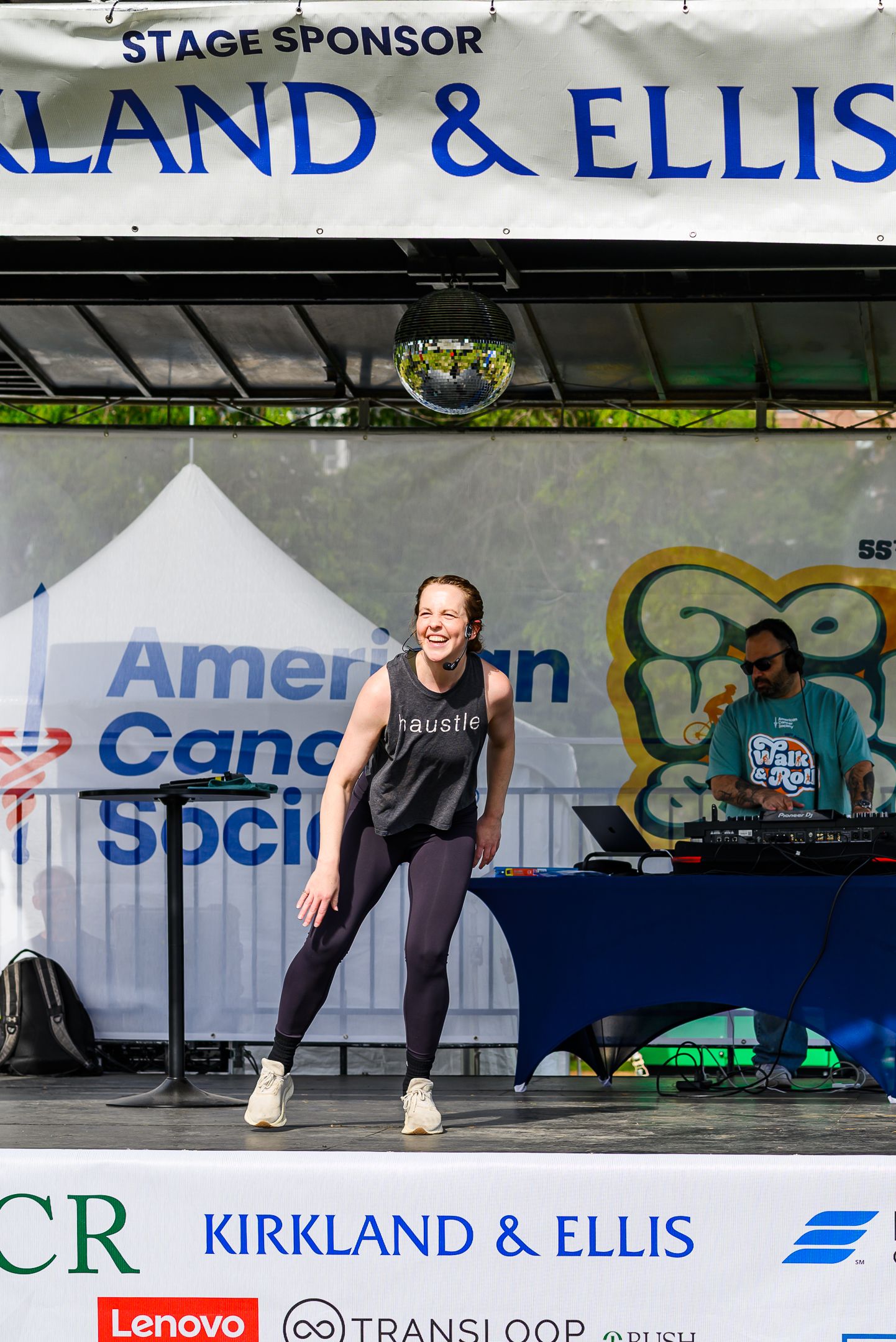 Fitness instructor in hustle tank top dancing on sponsored stage at American Cancer Society event.