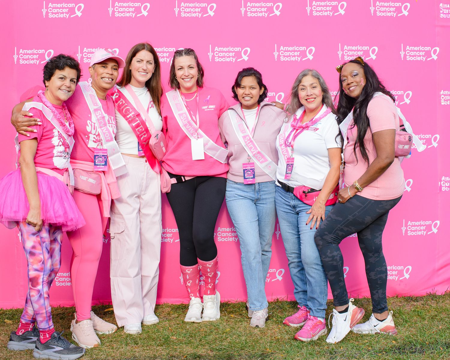 Row of people in pink and casual attire pose together against American Cancer Society branded wall.