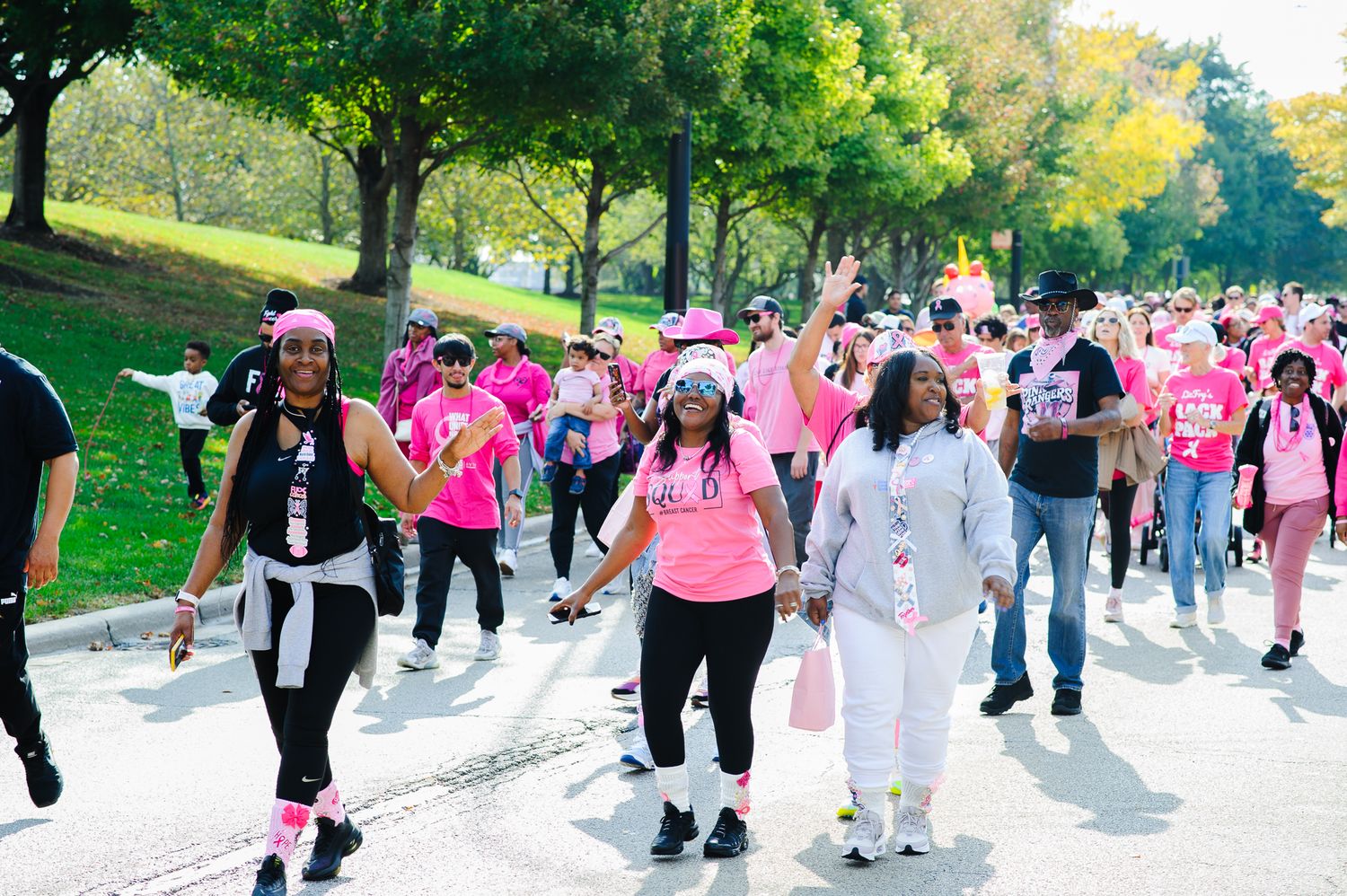 Large group of people wearing pink shirts walking together in a park during a breast cancer awareness event.