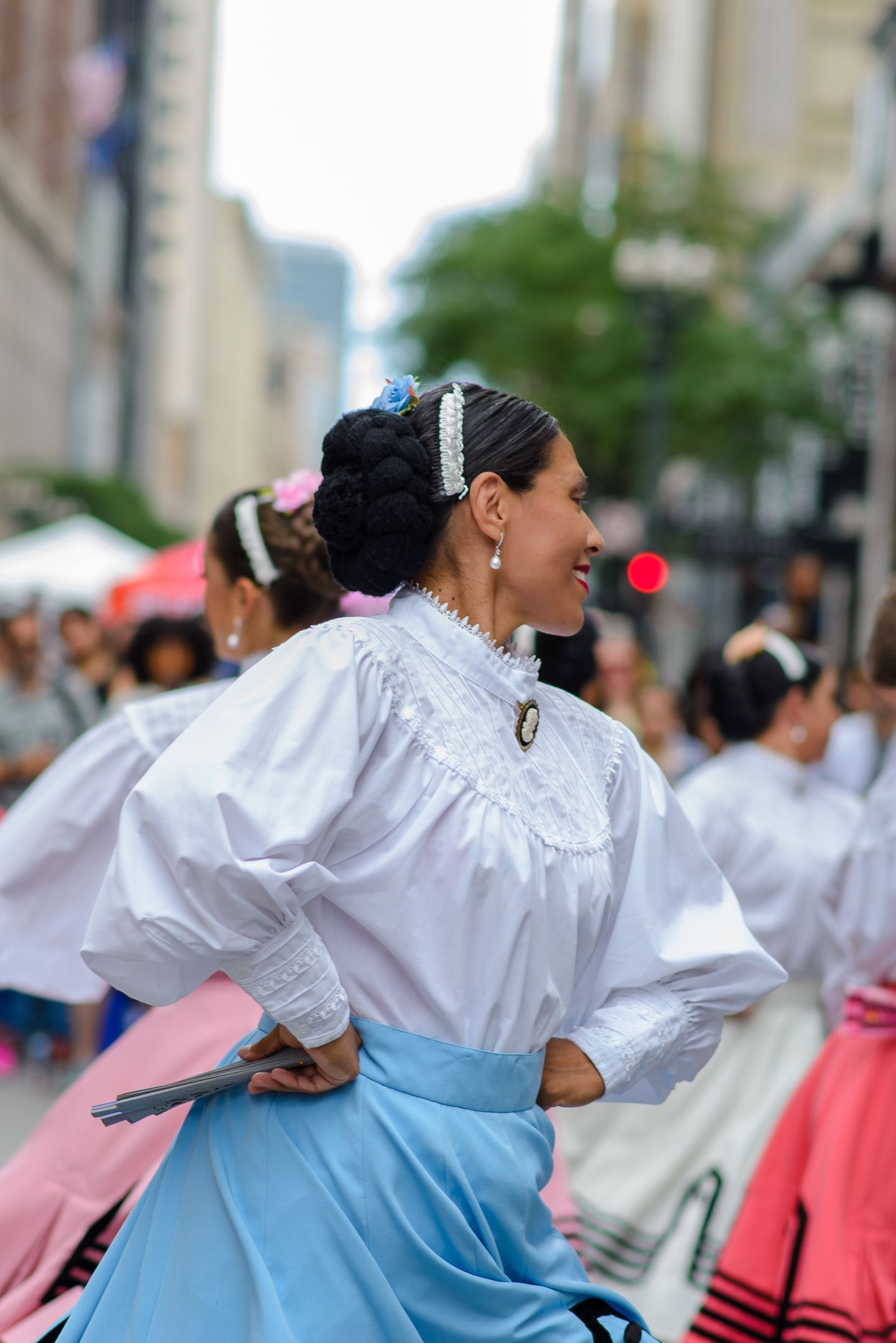 Dancers in white blouses and light blue skirts perform traditional folk dances at an outdoor cultural festival.