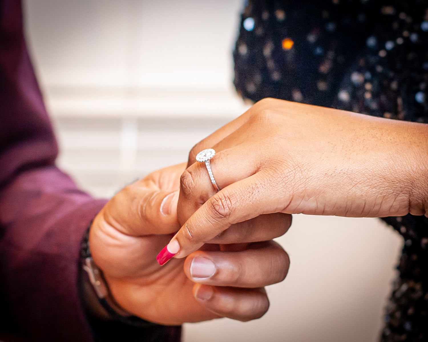 Close-up of a person placing a diamond engagement ring on a woman's finger with pink nails.