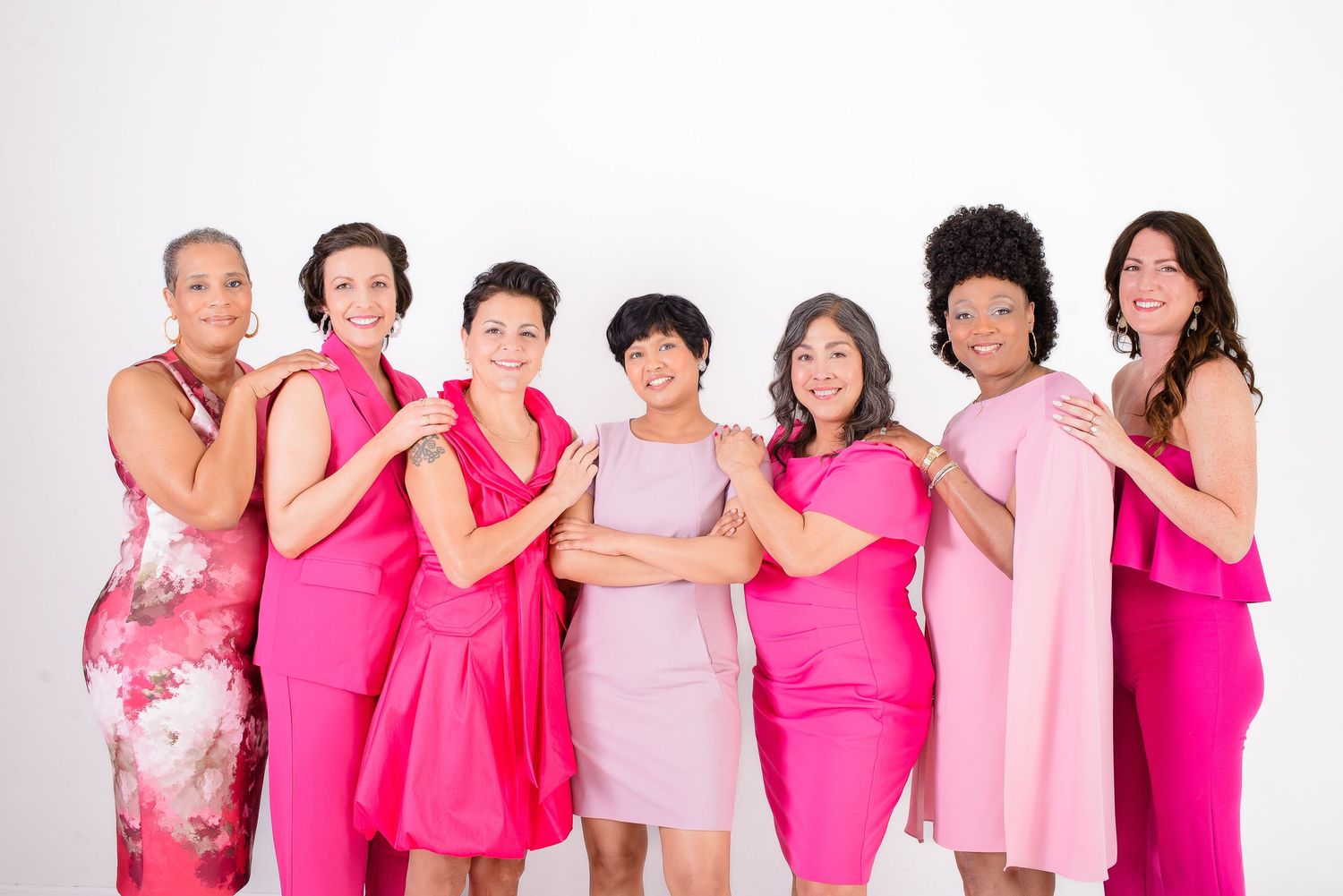A group of people wearing various shades of pink clothing stand together in solidarity against breast cancer.