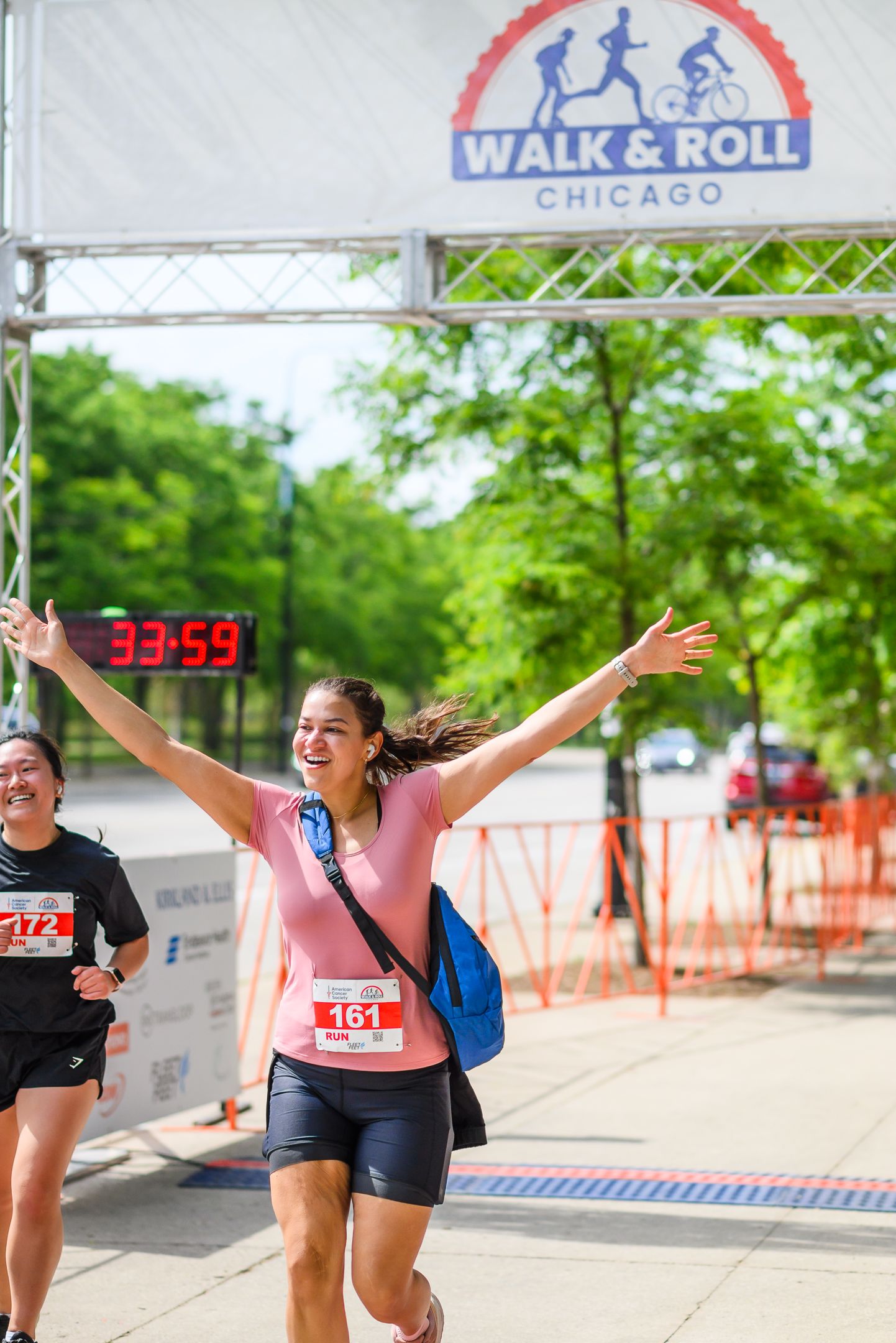 Jubilant woman raises arms crossing Walk & Roll Chicago finish line at 33:59 at cancer charity event.