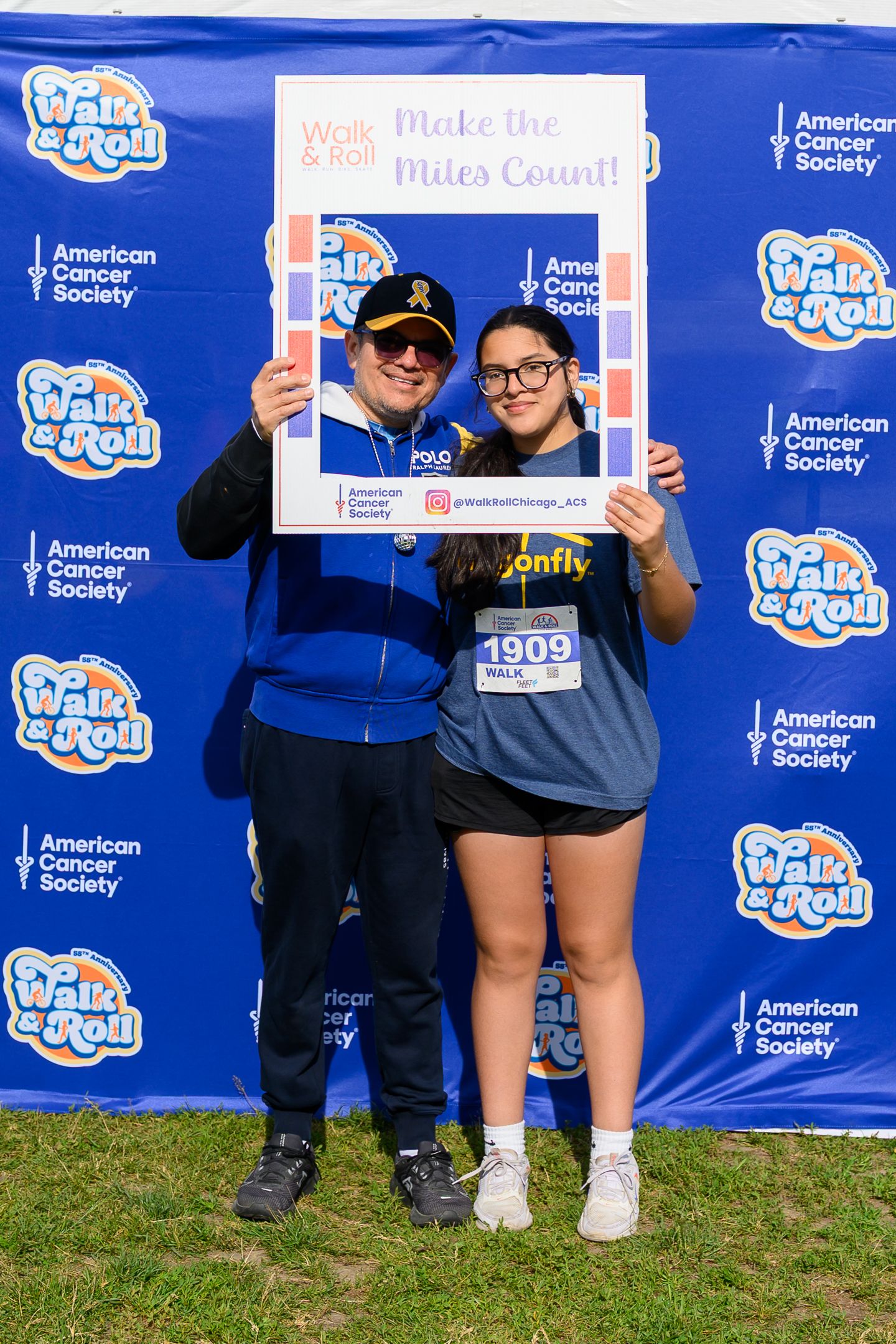 Two participants pose with a Walk & Roll American Cancer Society fundraiser photo frame at a charity walk event.