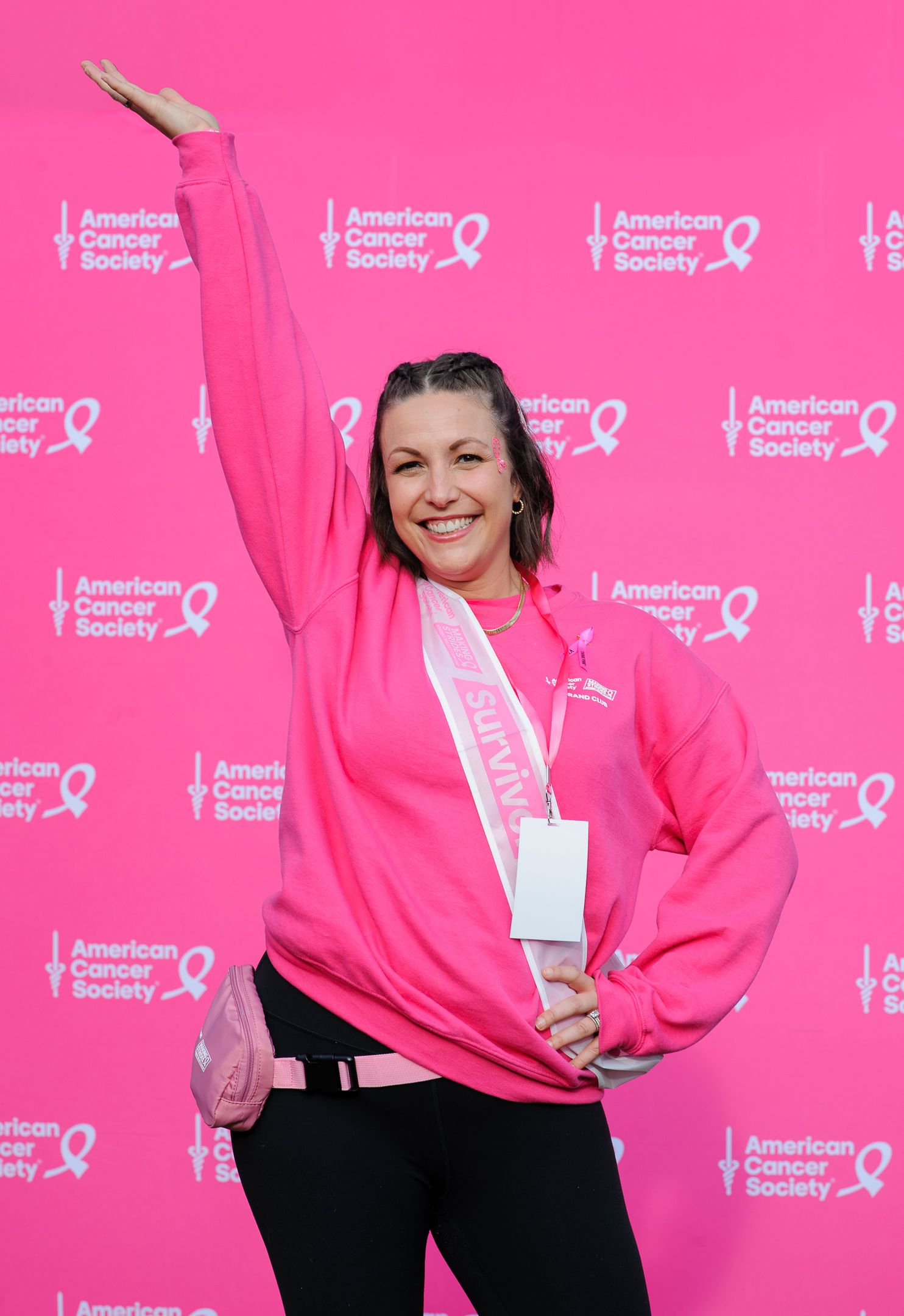 Participant in pink sweatshirt strikes enthusiastic pose at American Cancer Society event.