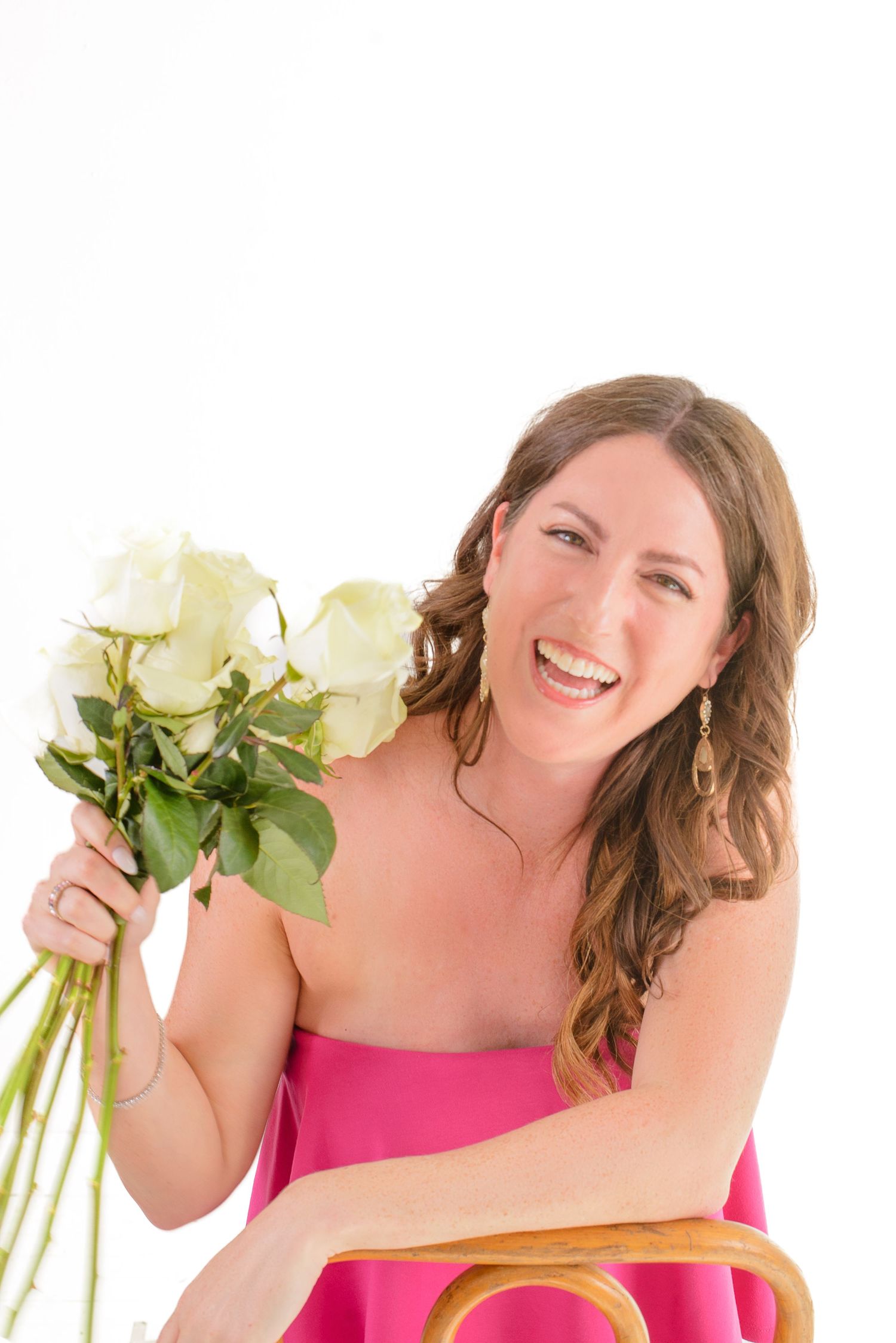 A person in a pink top holds a bouquet of white roses while smiling warmly against a white background.