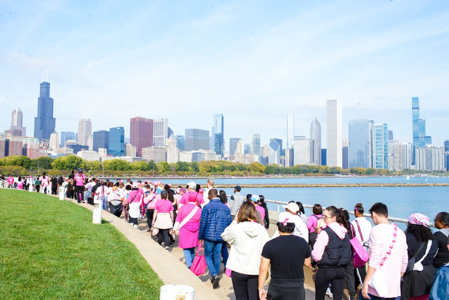 Crowd of people walking along Chicago's lakefront path with the city skyline visible in the background.