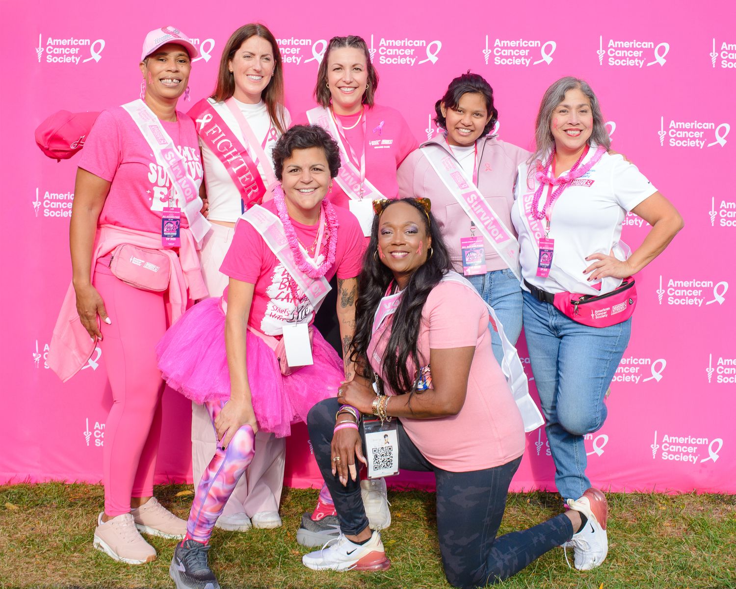 Cancer awareness event participants gather for group photo with pink branded backdrop.